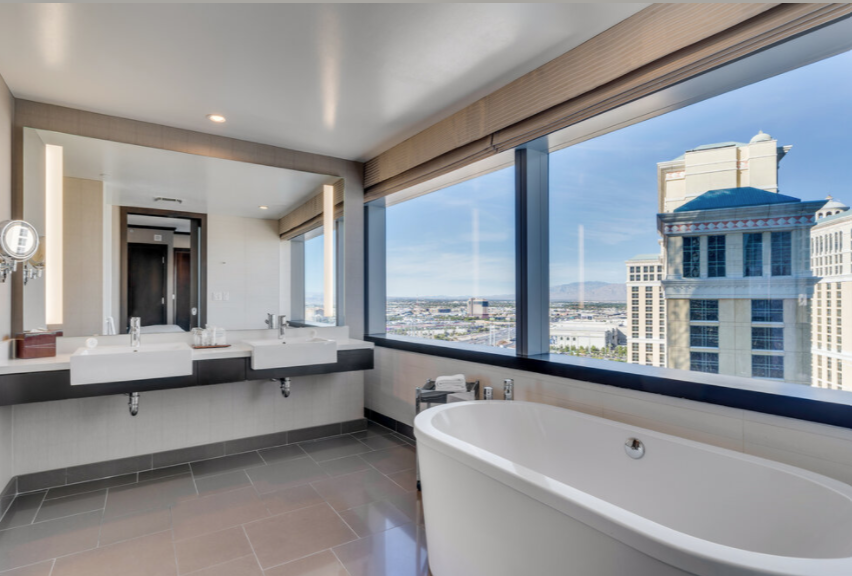 Modern bathroom with double vanity, soaking tub, and large windows overlooking city buildings