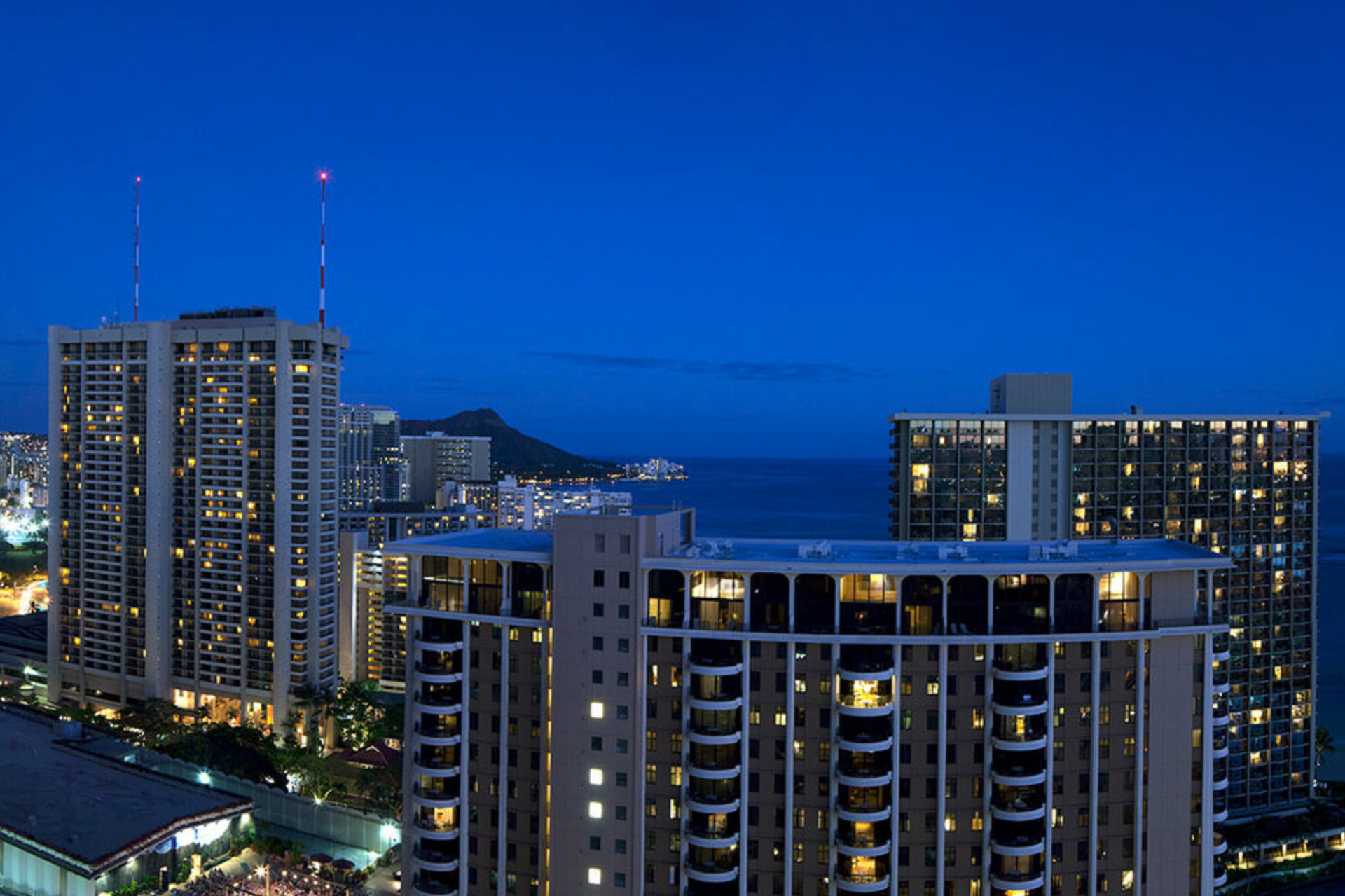 City skyline at dusk with illuminated high-rise buildings against a deep blue sky.
