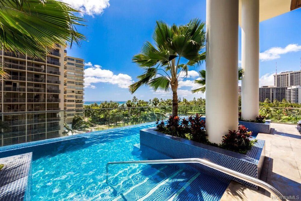Tropical resort pool with blue water, palm trees, and ocean-view high-rises under a bright sky