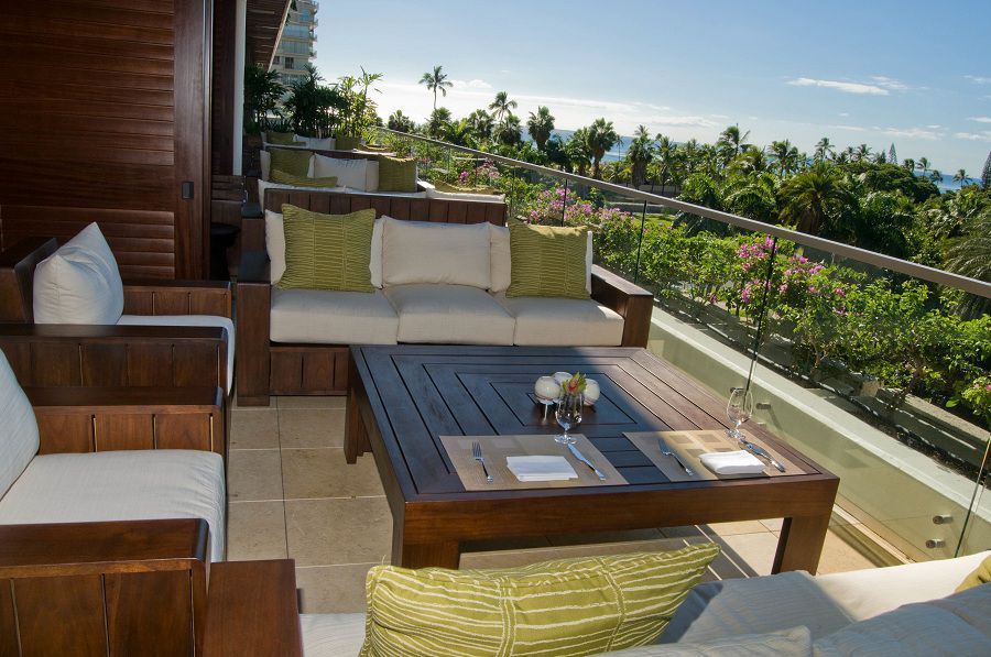 Outdoor patio with wicker seating, coffee table, and ocean-view greenery in bright sunlight