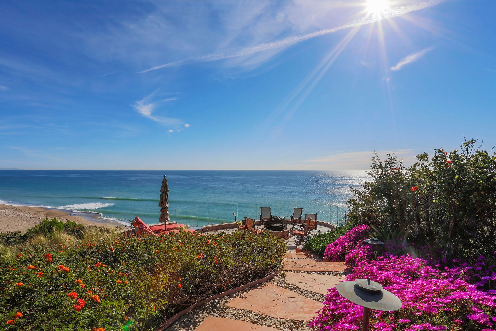 Sunny coastal garden path with colorful flowers overlooking the ocean under a bright blue sky.