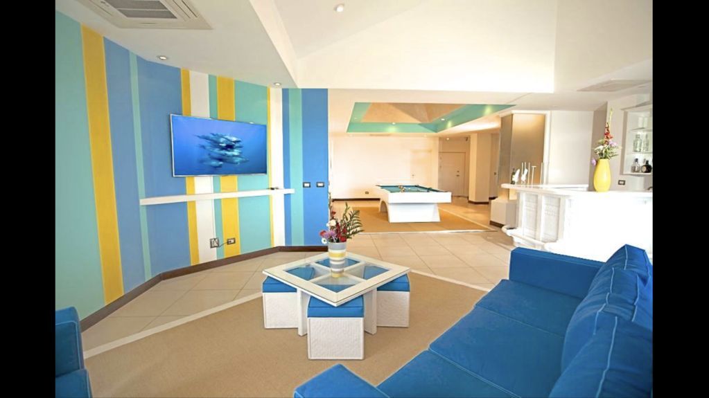 Bright living room with blue sofa, striped accent wall, TV, and a bedroom area in the background