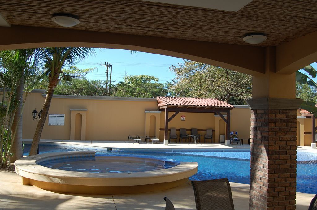 Covered resort pool with a round hot tub, blue water, and lounge area under a tiled patio.