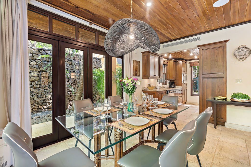 Modern dining room with glass table, white chairs, wood ceiling, and large windows to a garden