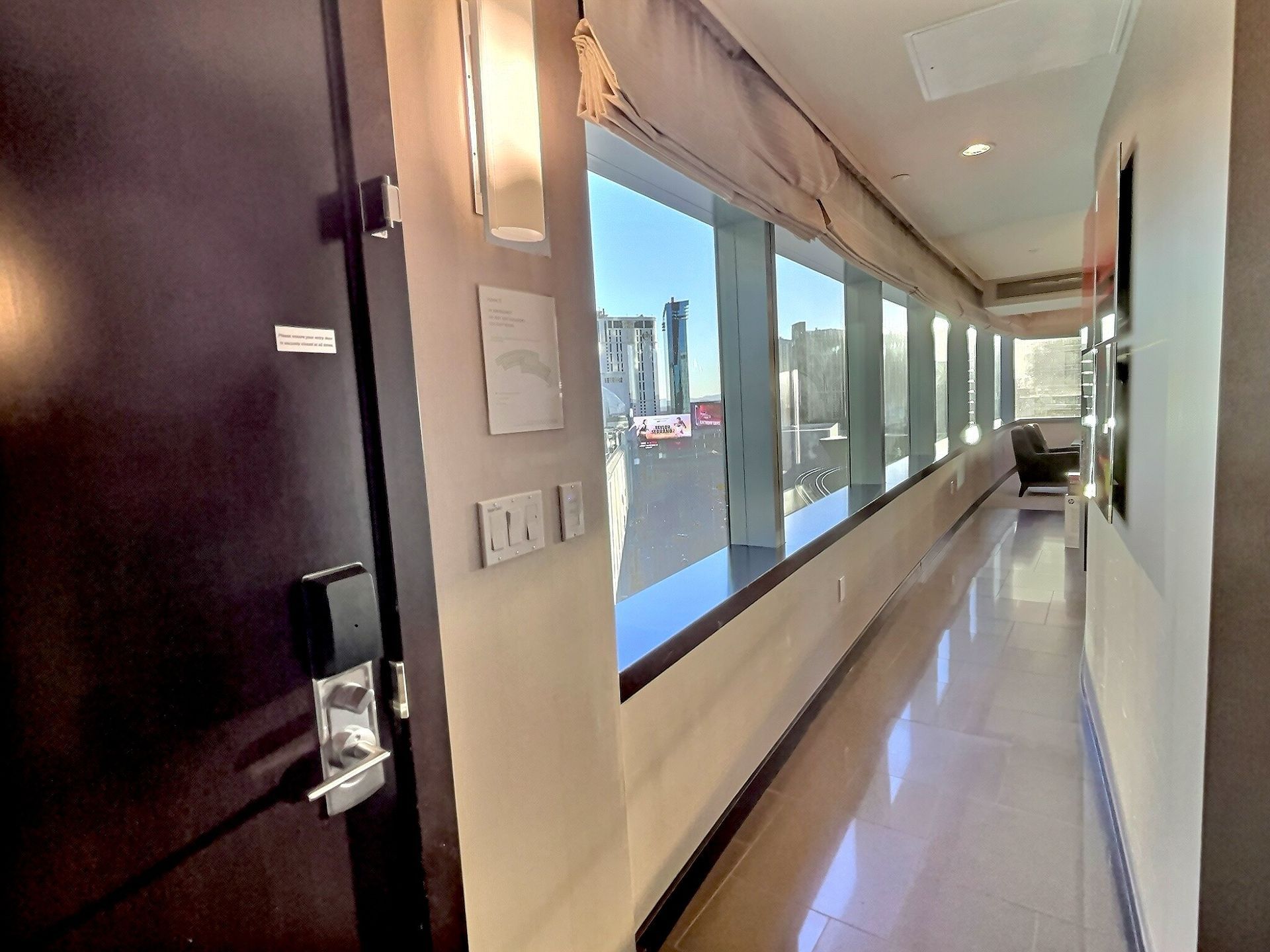 Office hallway with large windows, glossy floor, and a dark door on the left