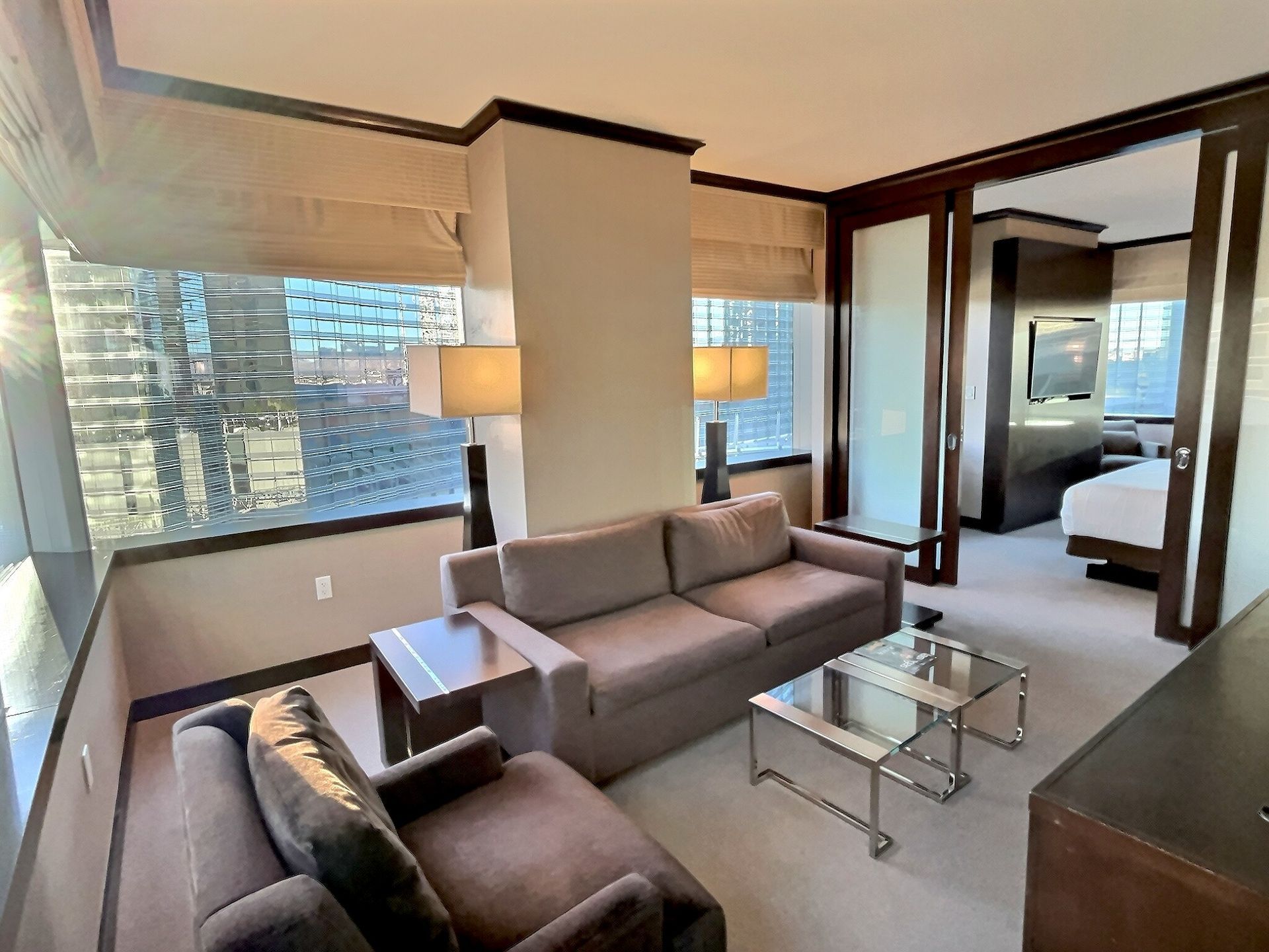 Modern hotel suite with gray sofa, chairs, glass coffee table, and large windows