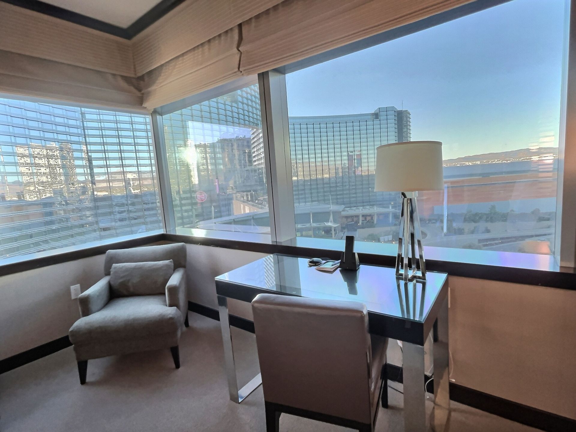 Modern hotel room with desk and chair by large windows overlooking water and buildings