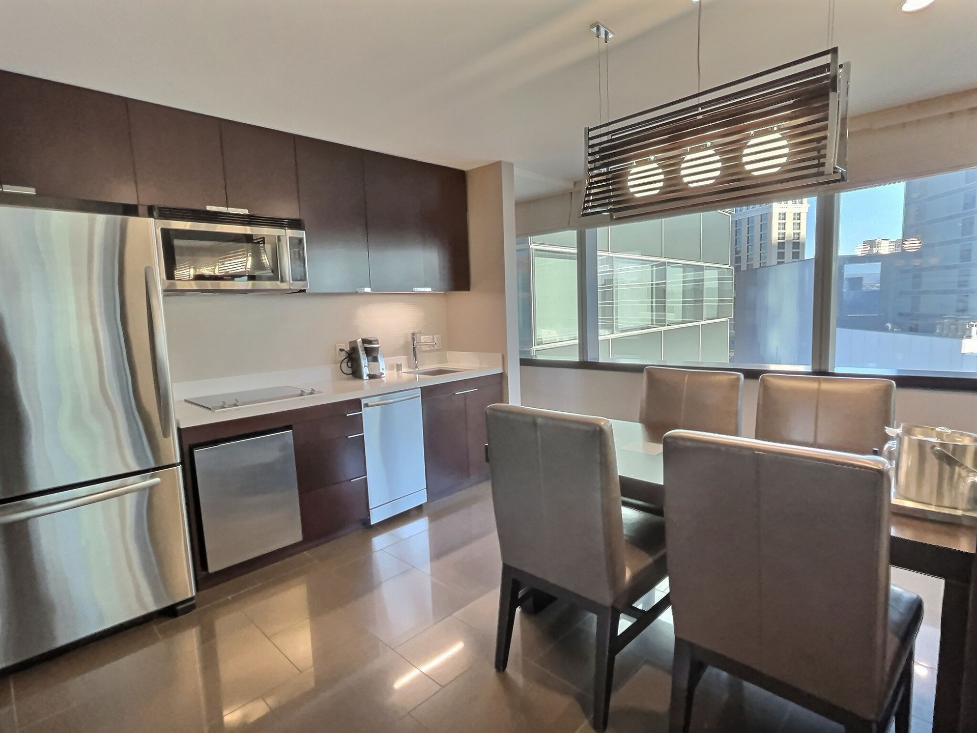 Modern kitchen and dining area with stainless steel appliances, dark cabinets, and a glass-top table by a window