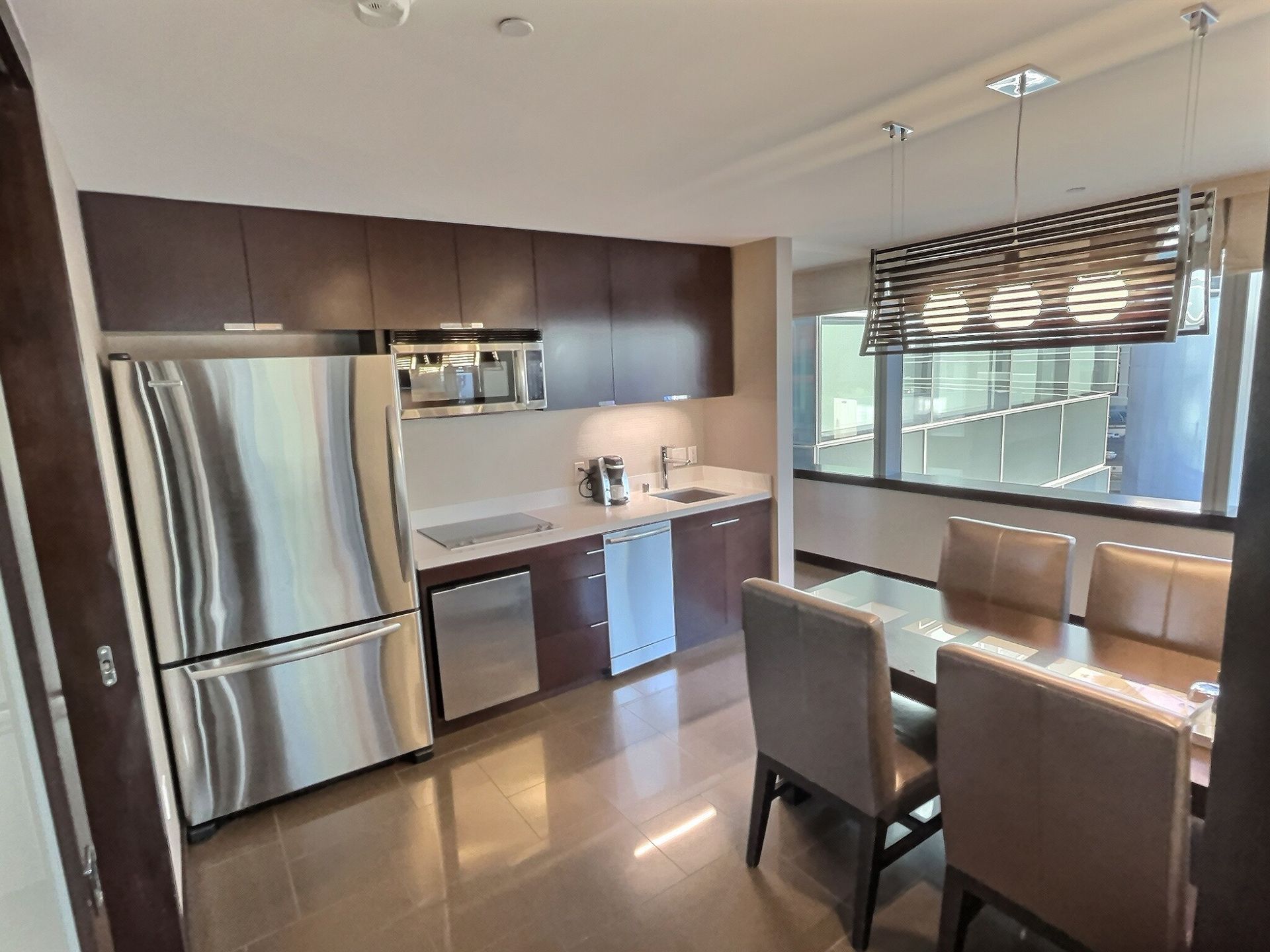 Modern kitchen with stainless steel appliances, dark cabinets, and a small dining table by a window.
