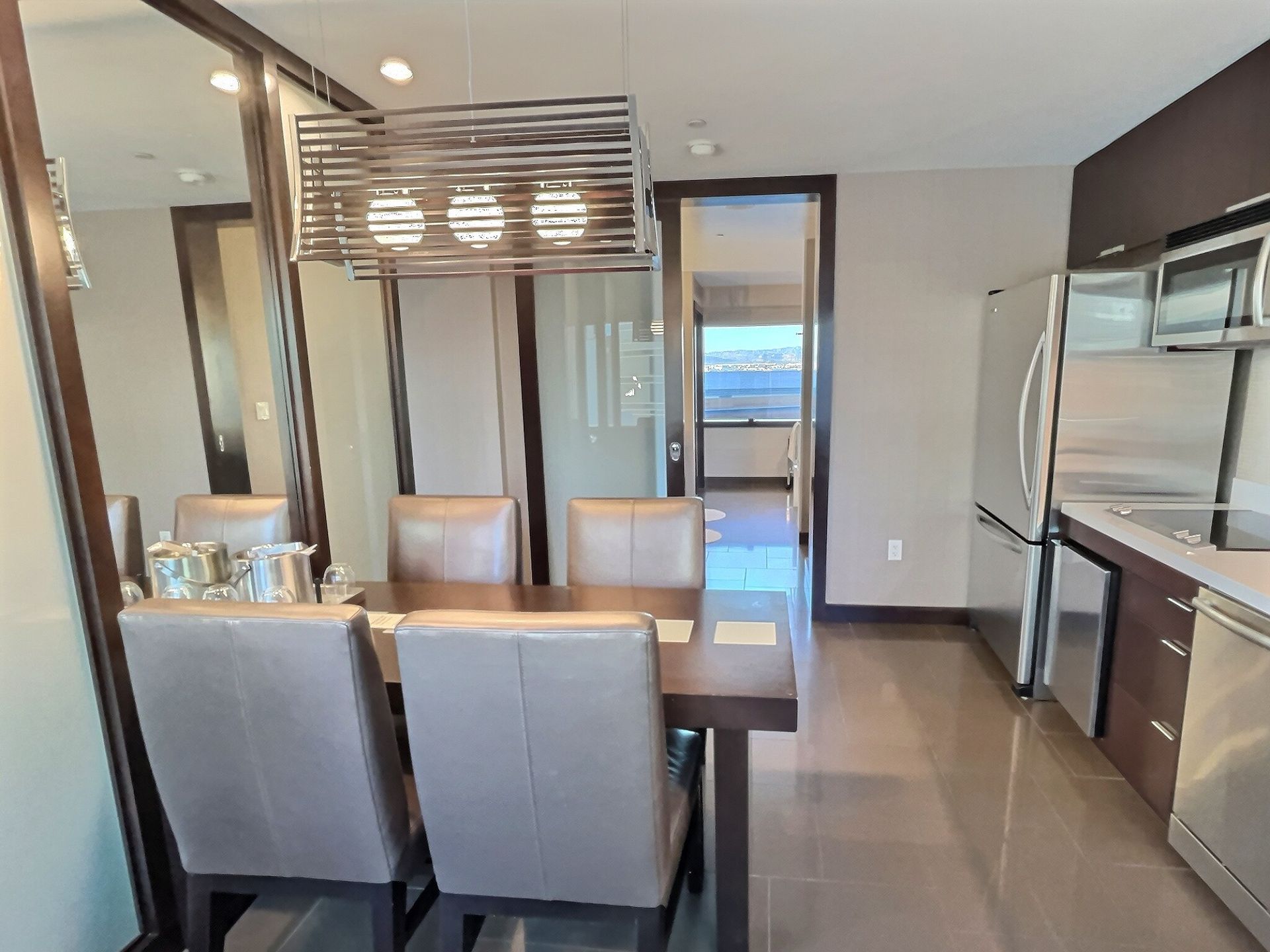 Modern kitchen-dining area with gray chairs, dark cabinetry, island pendant lights, and stainless-steel appliances