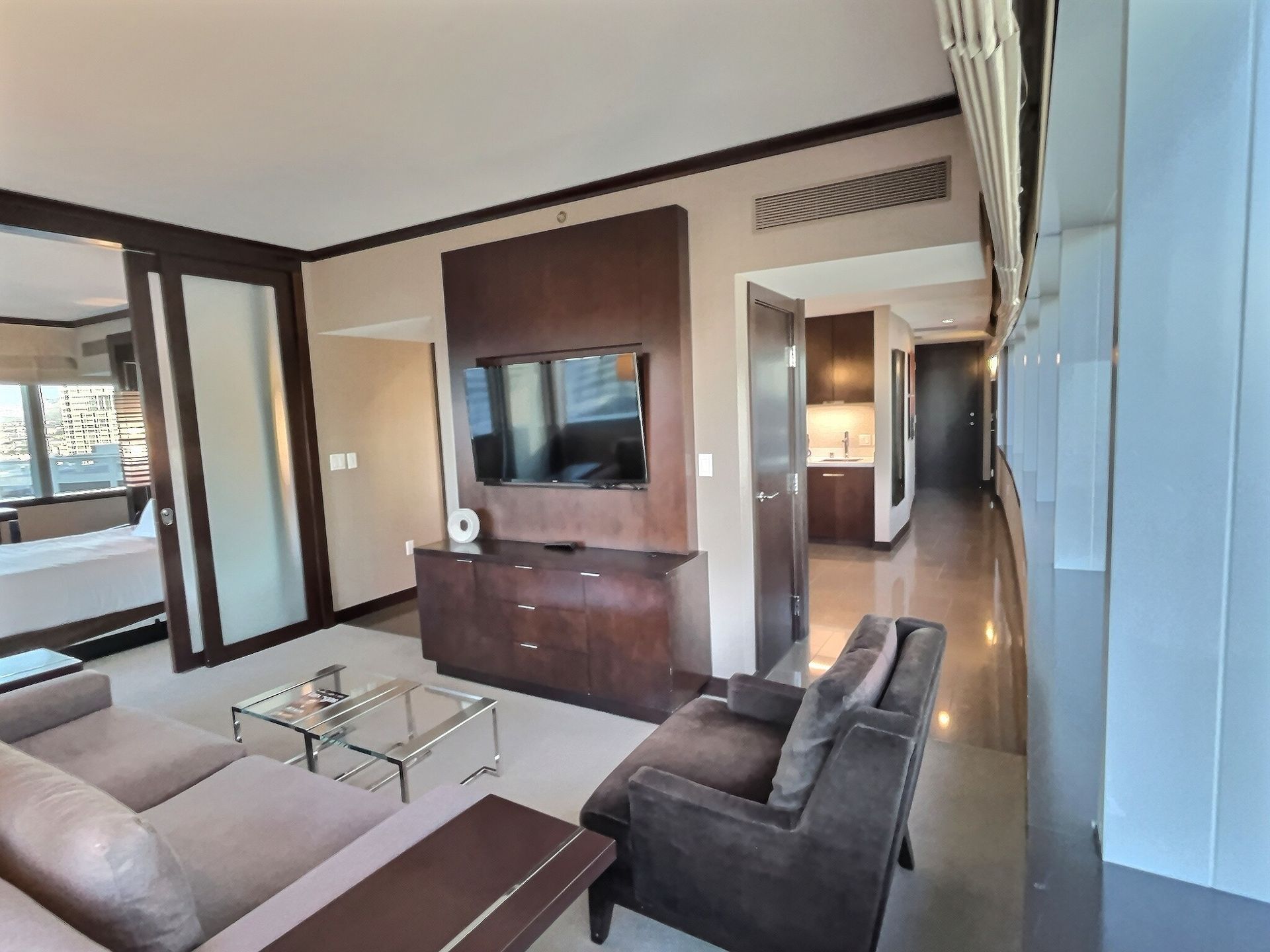 Modern living room with sofa, glass coffee table, wall-mounted TV, and hallway view