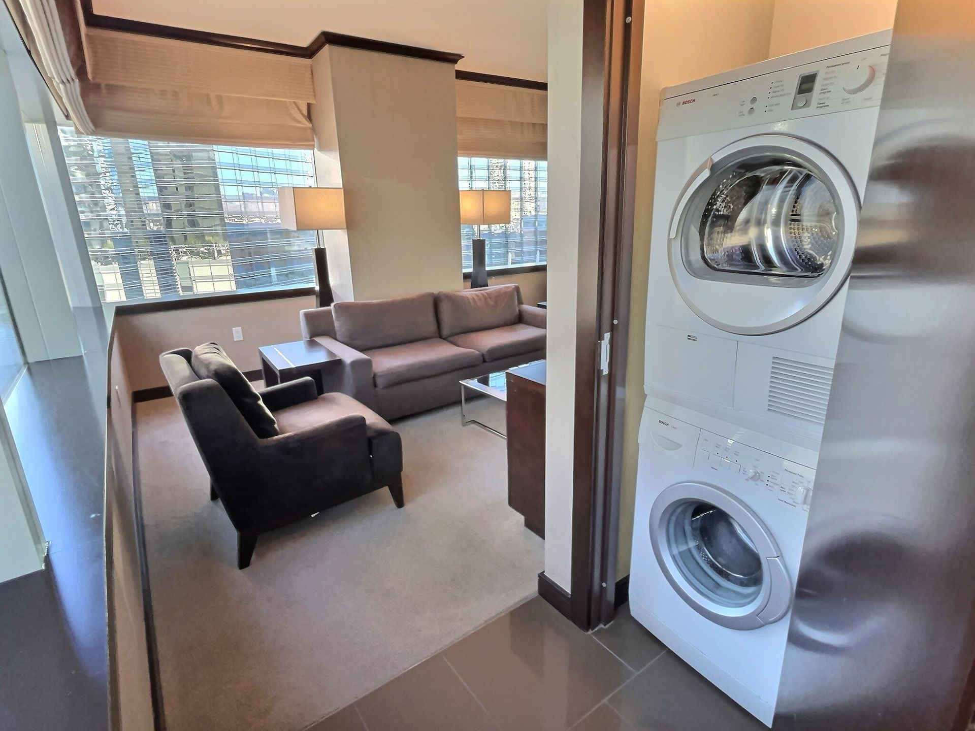 Living room with gray sofa, black chair, large windows, and stacked washer-dryer by the doorway