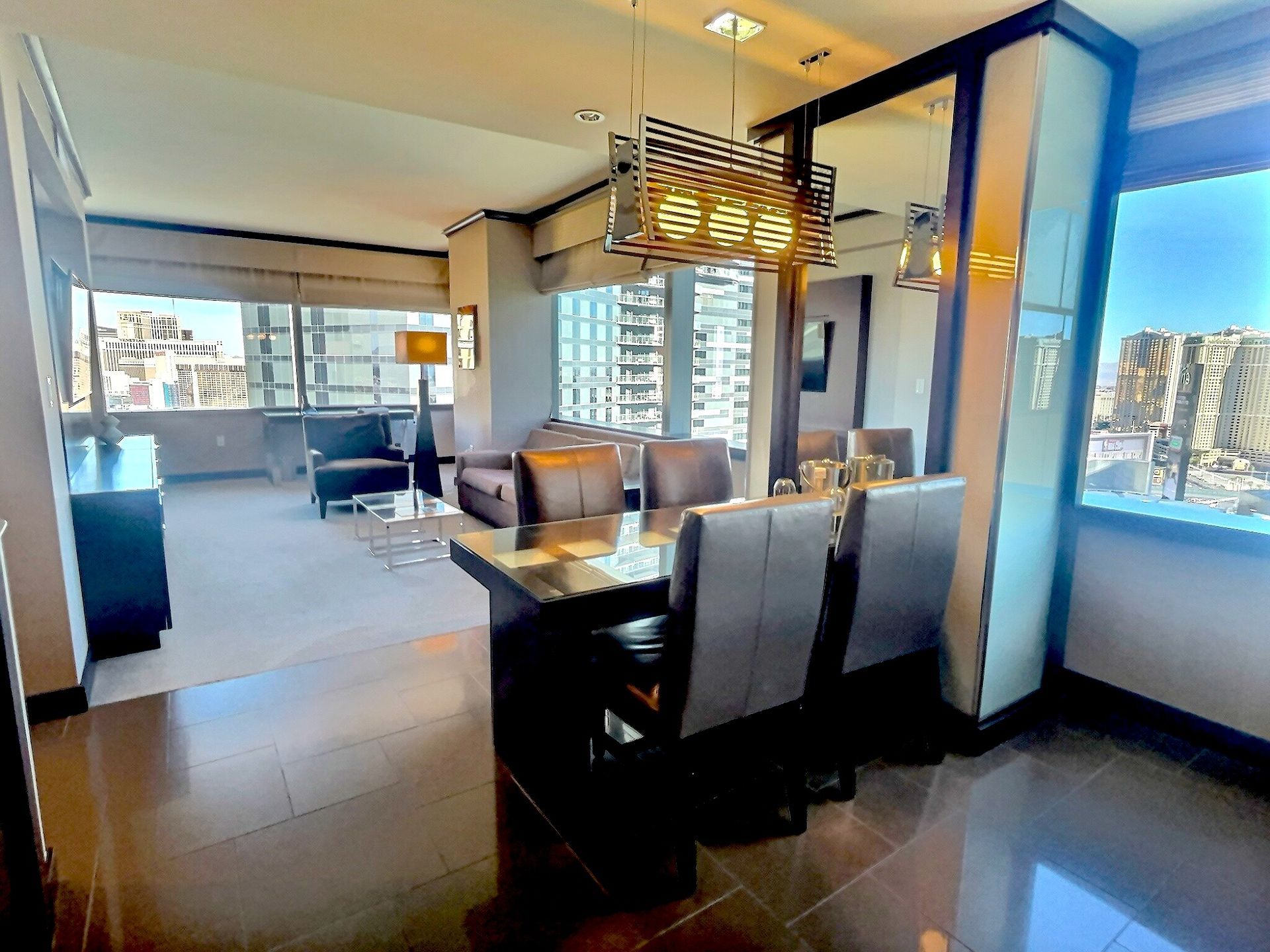 Modern dining and living room with large windows, dark chairs, and city views