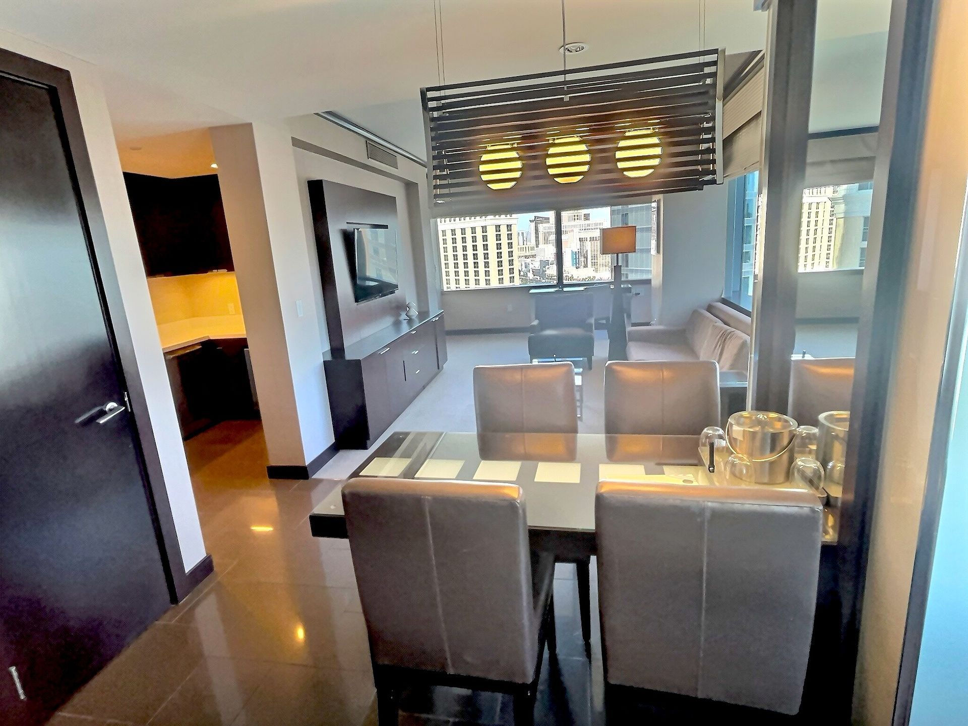 Modern dining room with glass table, white chairs, pendant lights, and balcony view