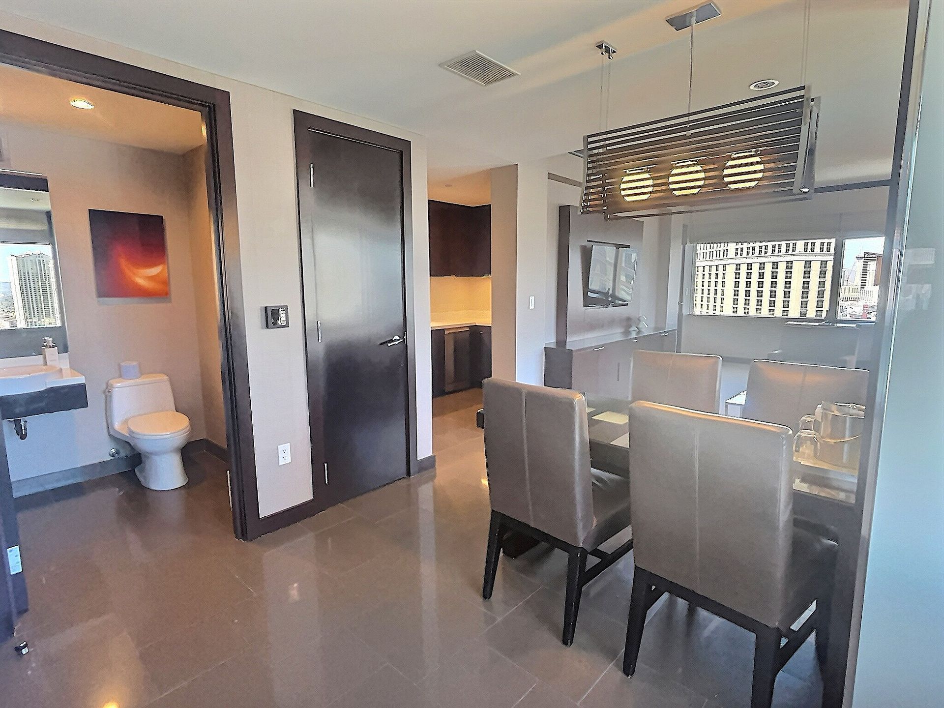 Modern apartment dining area with glass table, beige chairs, kitchen pass-through, and bathroom visible on the left