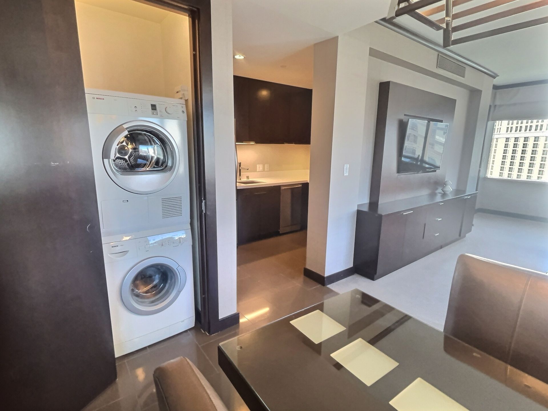 Modern apartment interior with stacked washer and dryer, hallway, and open kitchen beside a dining area