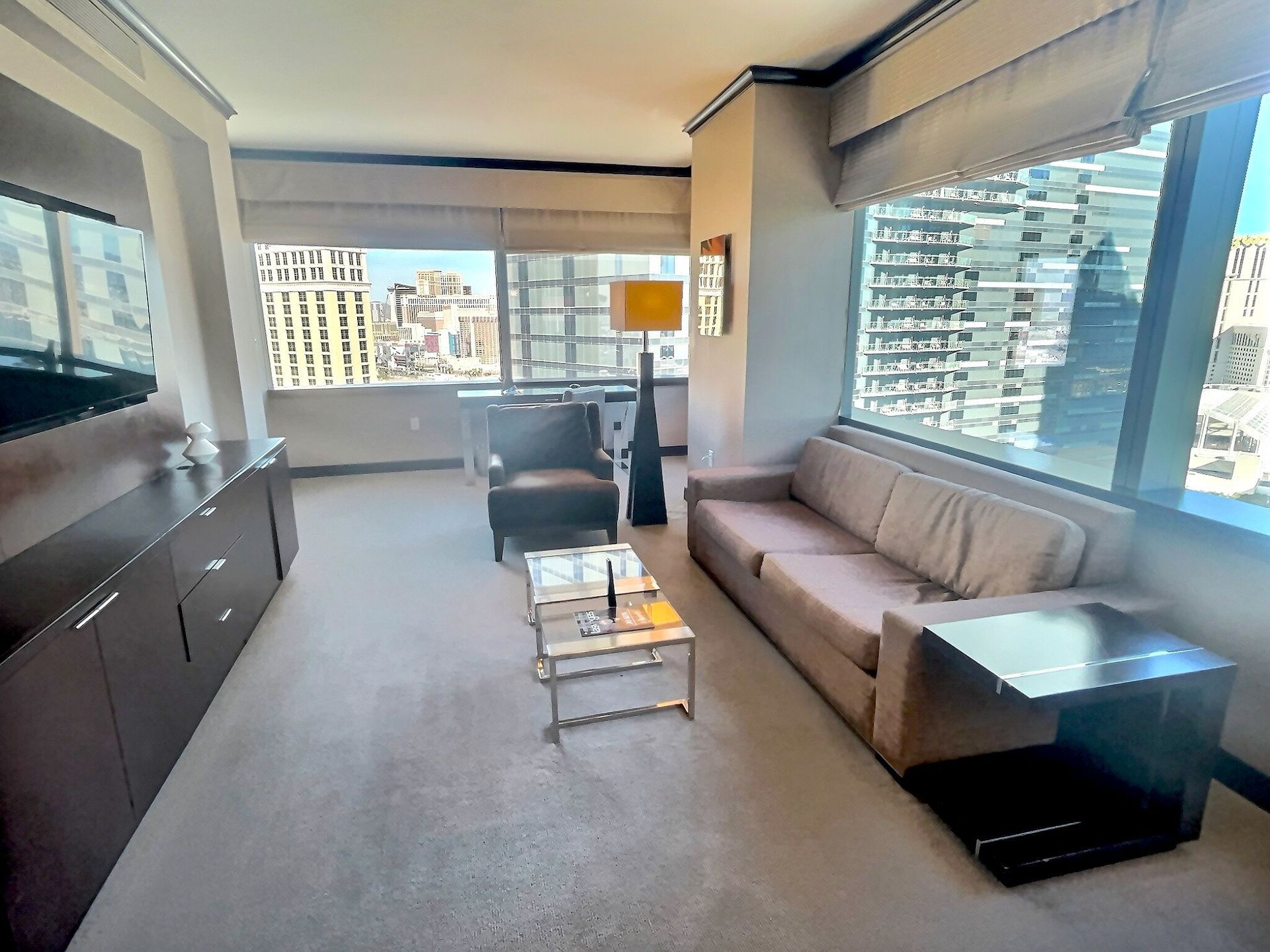 Bright living room with gray sofa, glass coffee table, and city views through large windows.