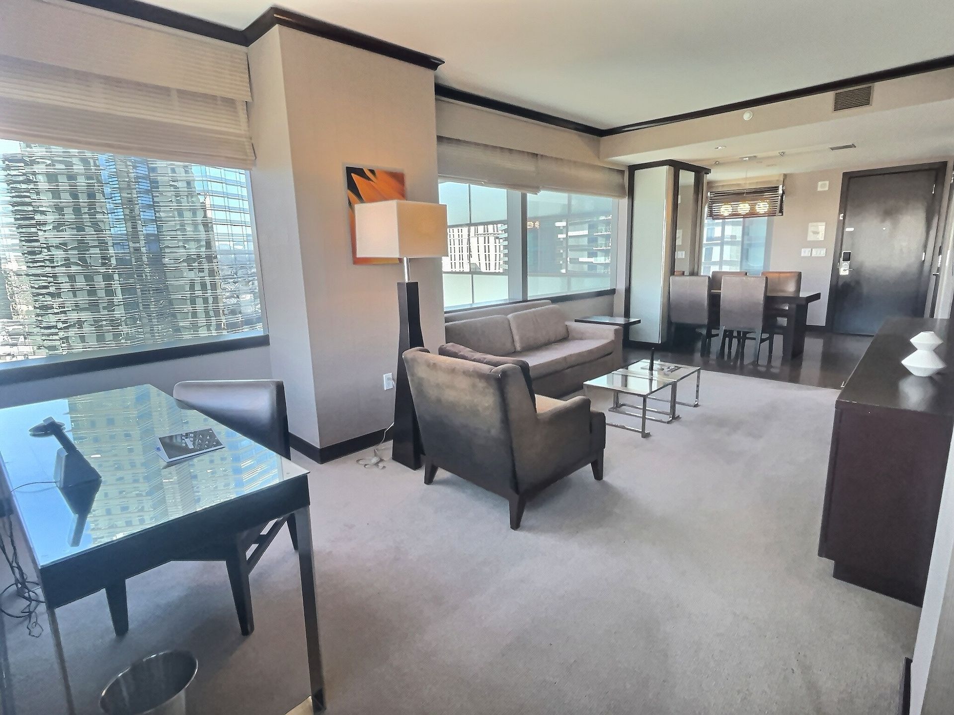 Bright living room with large windows, gray sofa and chairs, glass dining table, and city view