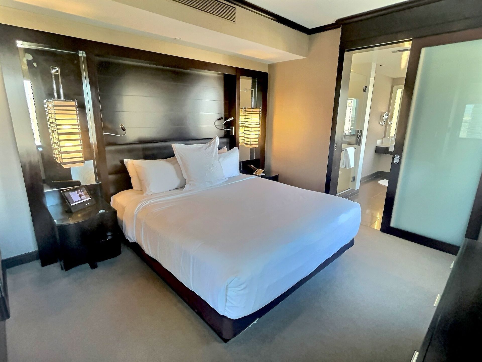 Modern bedroom with a white bed, dark wood headboard, and large windows at the back