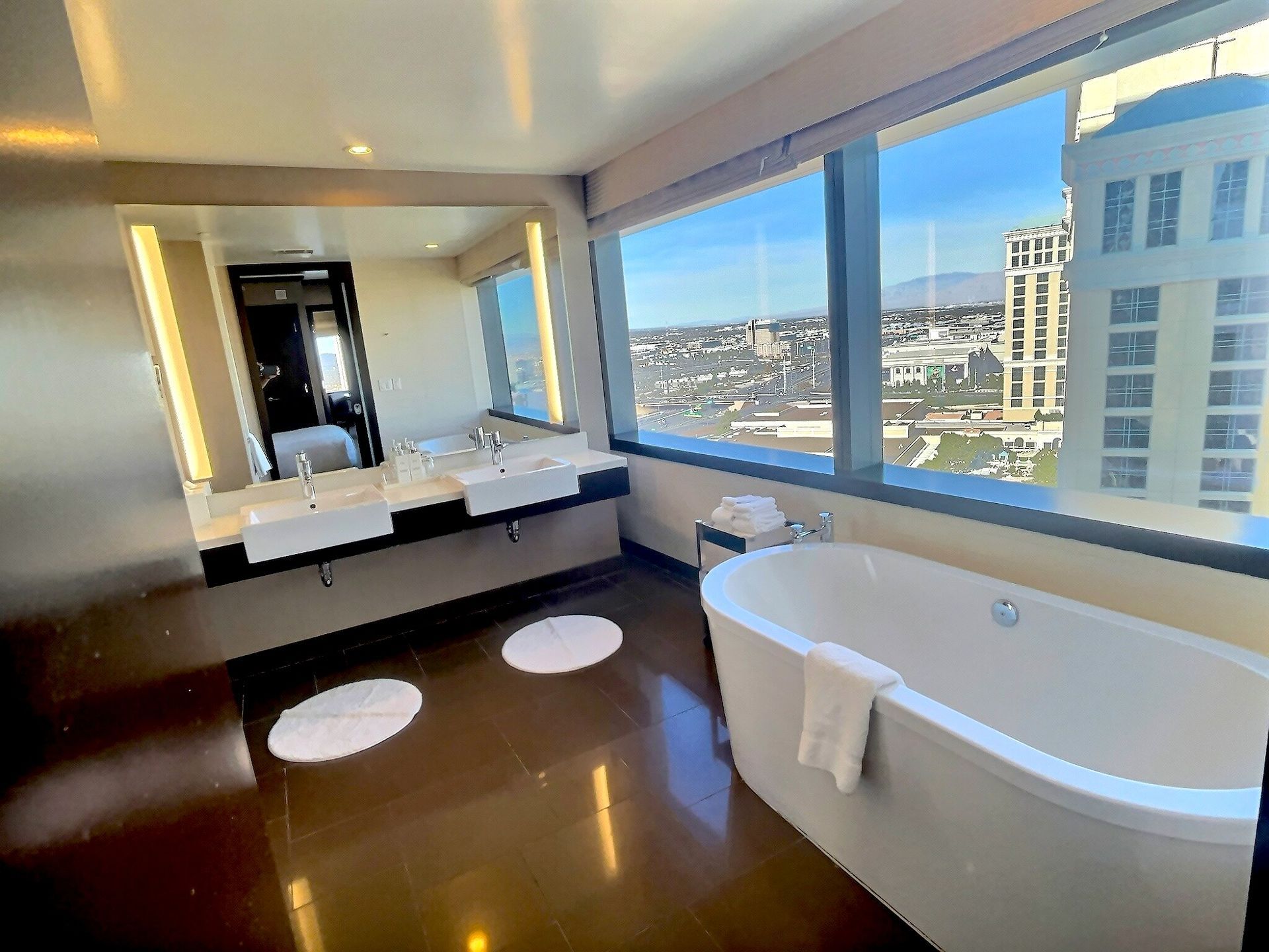 Modern bathroom with large windows, double vanity, and freestanding tub overlooking a city view