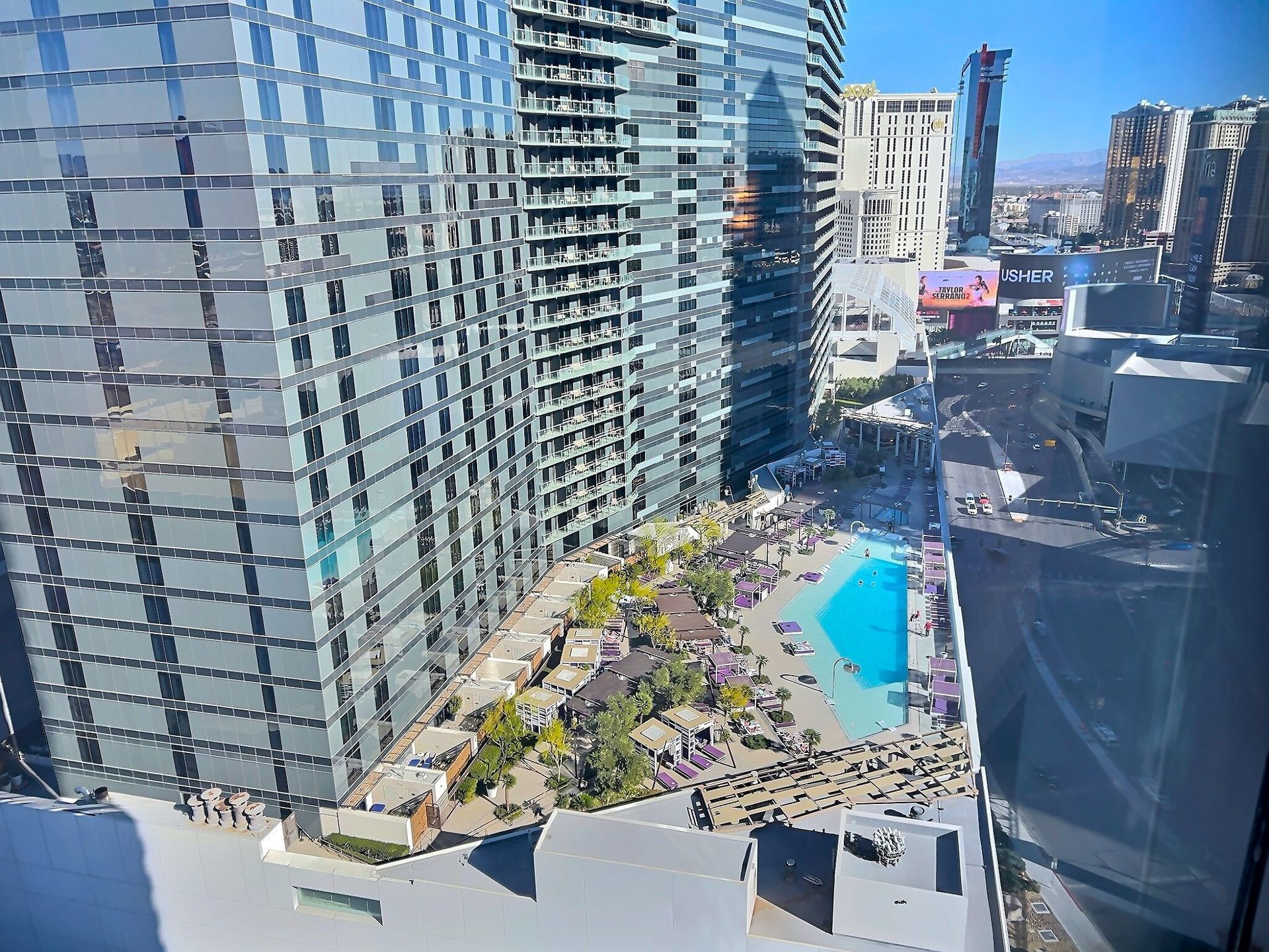 Downtown hotel pool deck with lounge chairs beside tall glass buildings and a city street below