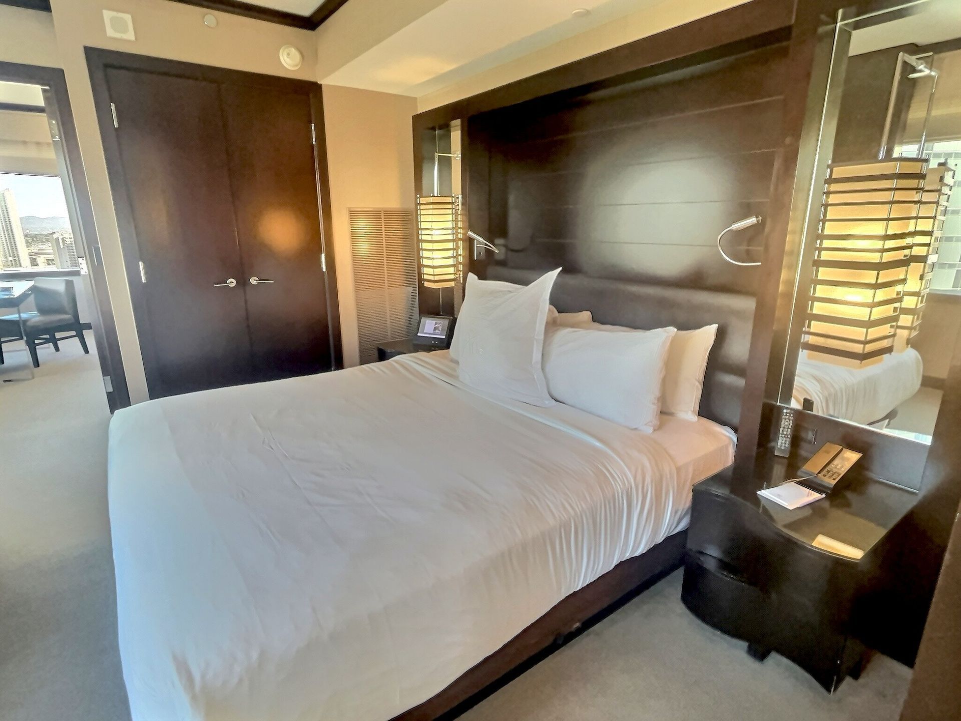 Modern hotel room with a neatly made bed, bedside lamps, and a dark wood headboard with mirror panels