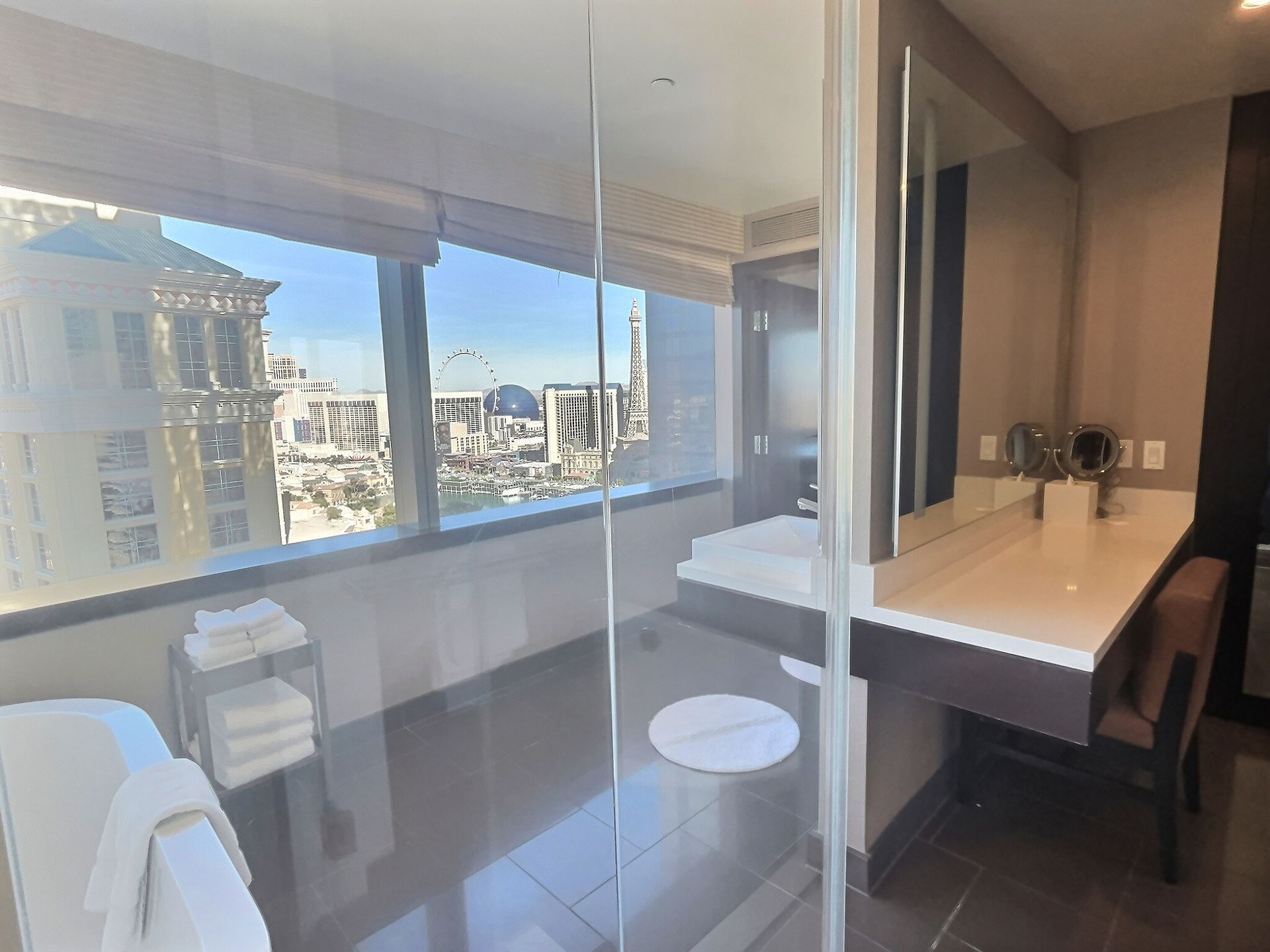 Bright hotel room with large corner window, city view, desk, chair, and bed