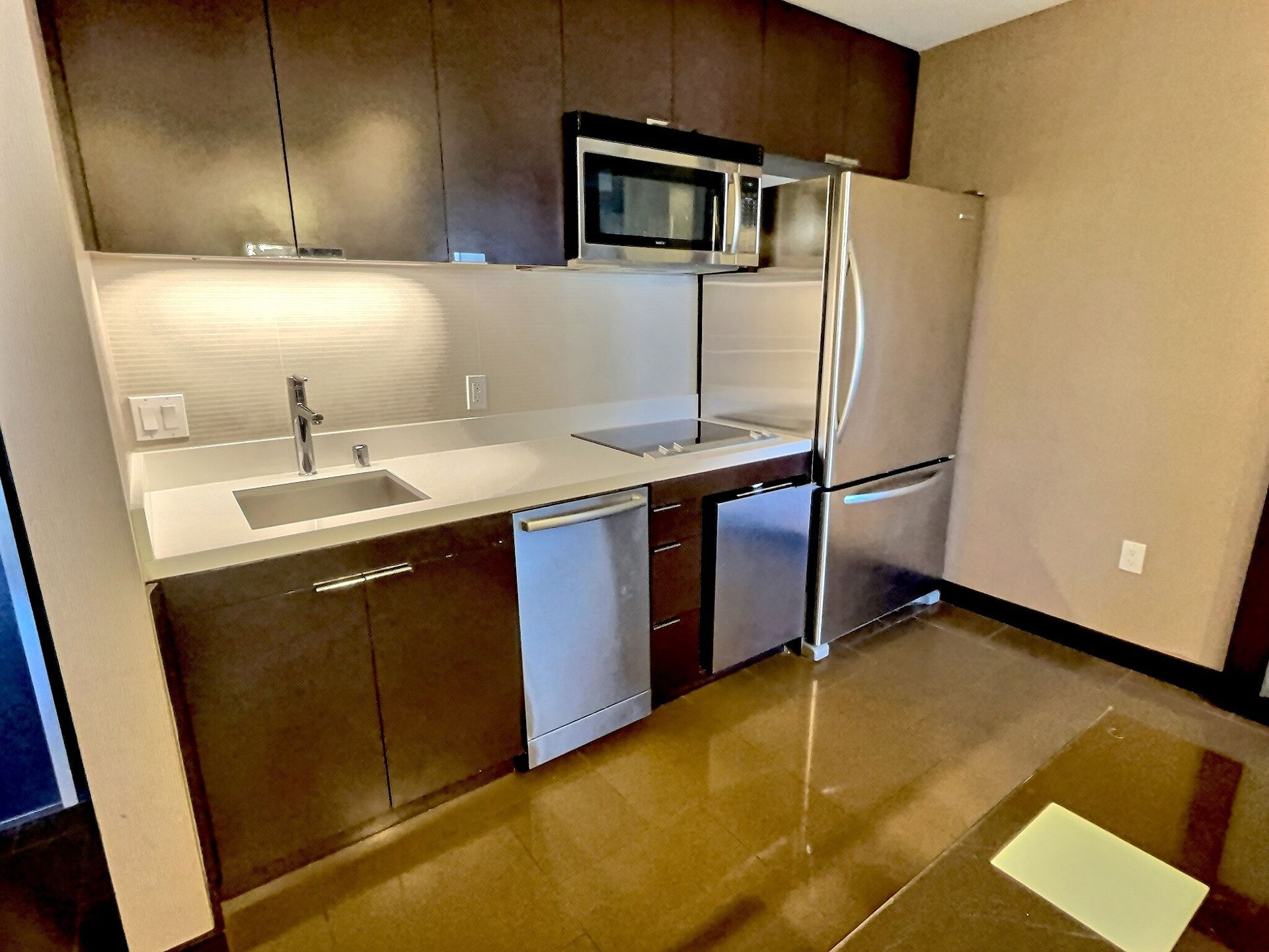 Small kitchen with dark wood cabinets, stainless appliances, white counters, and tan flooring.