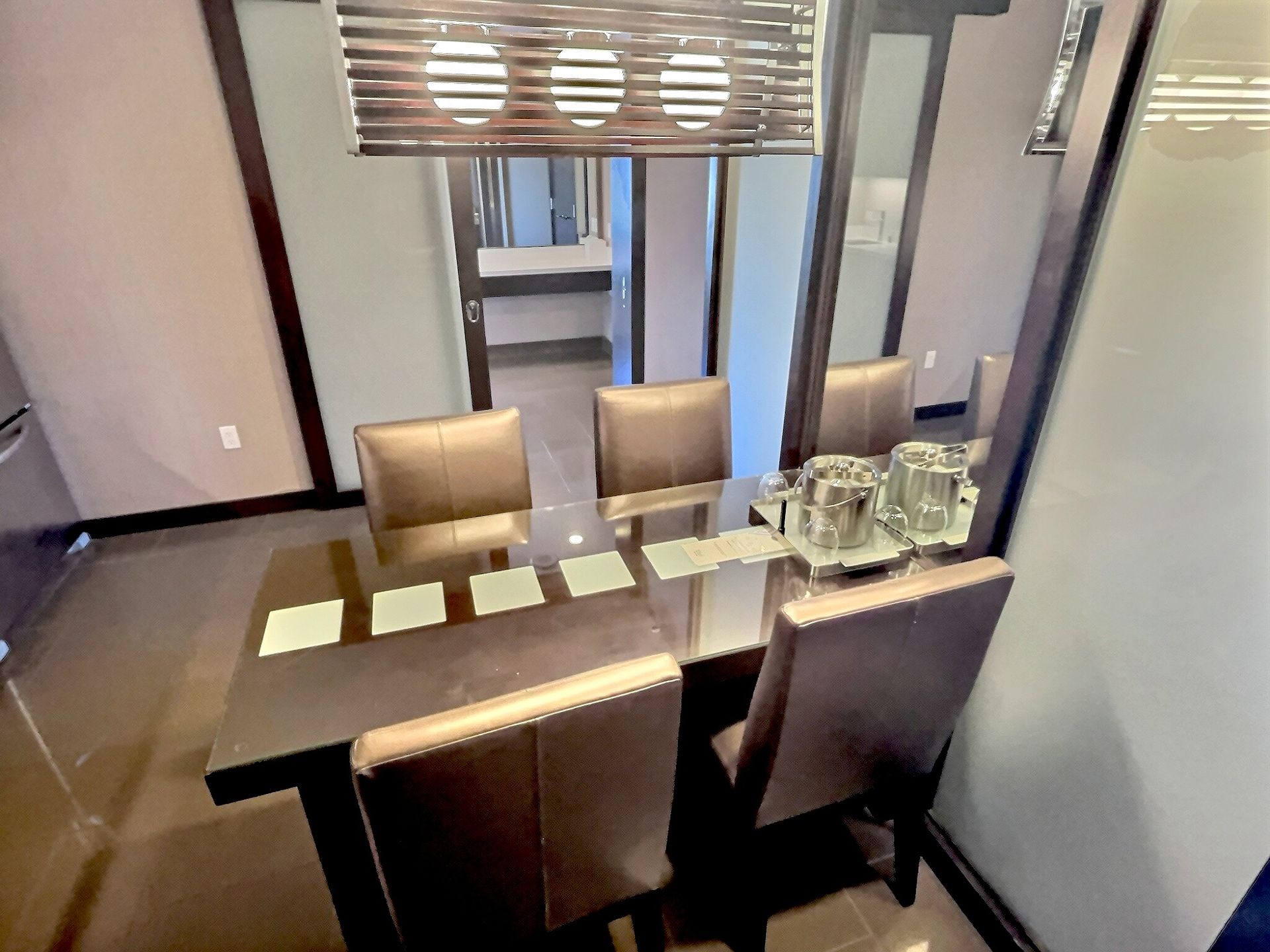 Dining room with glass-top table, four chairs, and place settings in a modern interior.