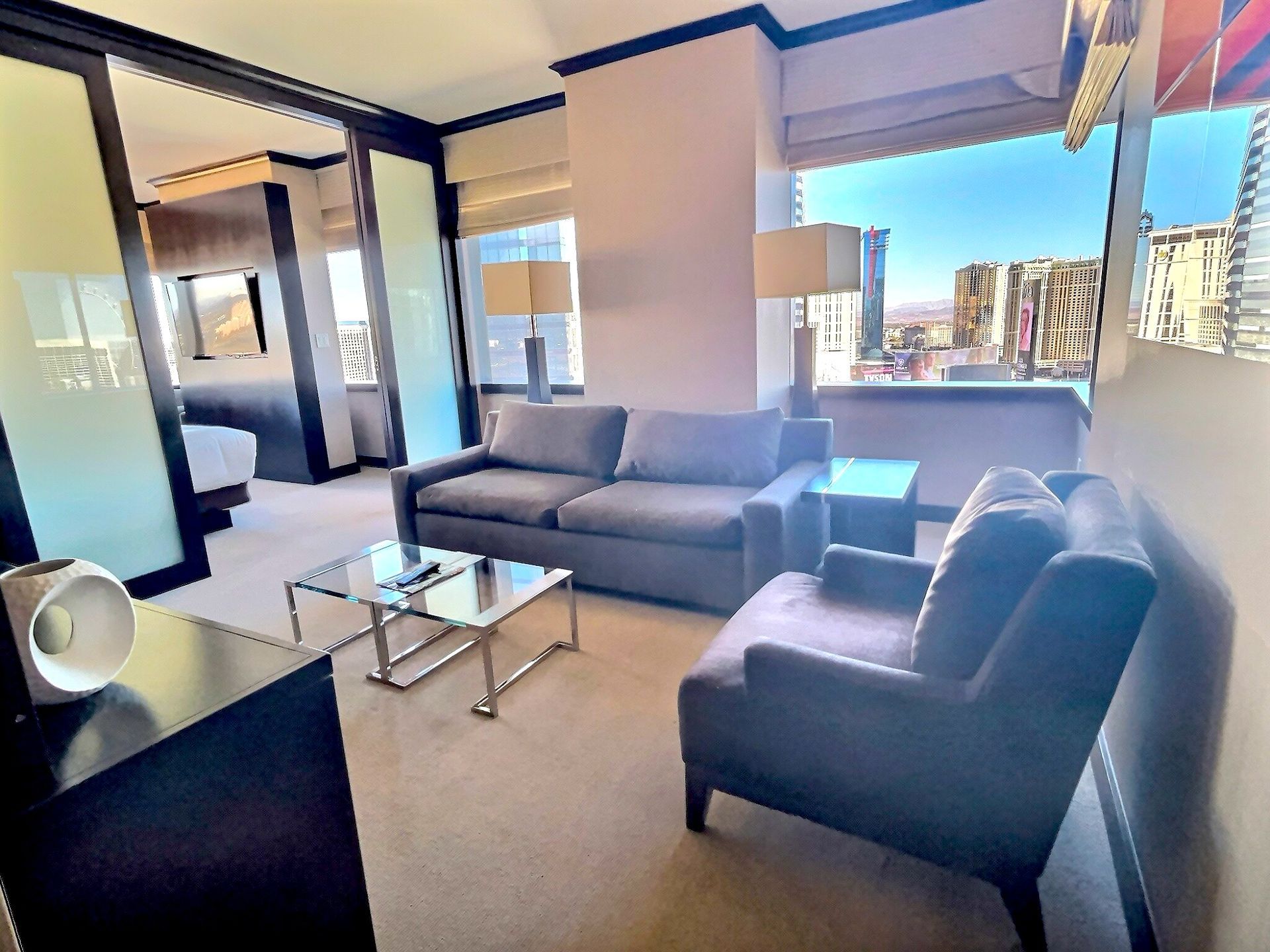 Modern living room with gray sofa, armchairs, glass coffee table, and large windows with city view