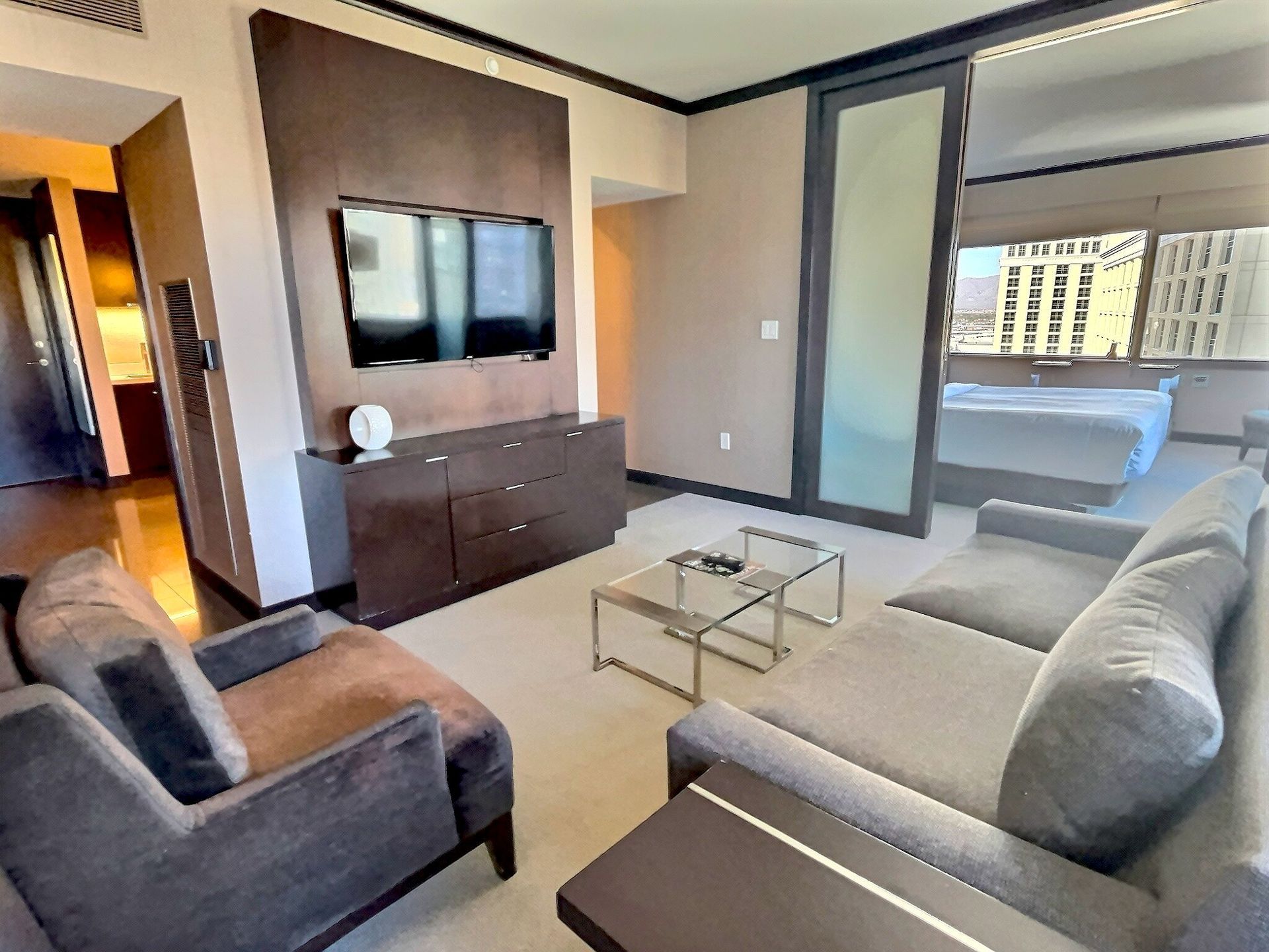 Modern living room with gray sofas, wall-mounted TV, glass coffee table, and balcony view