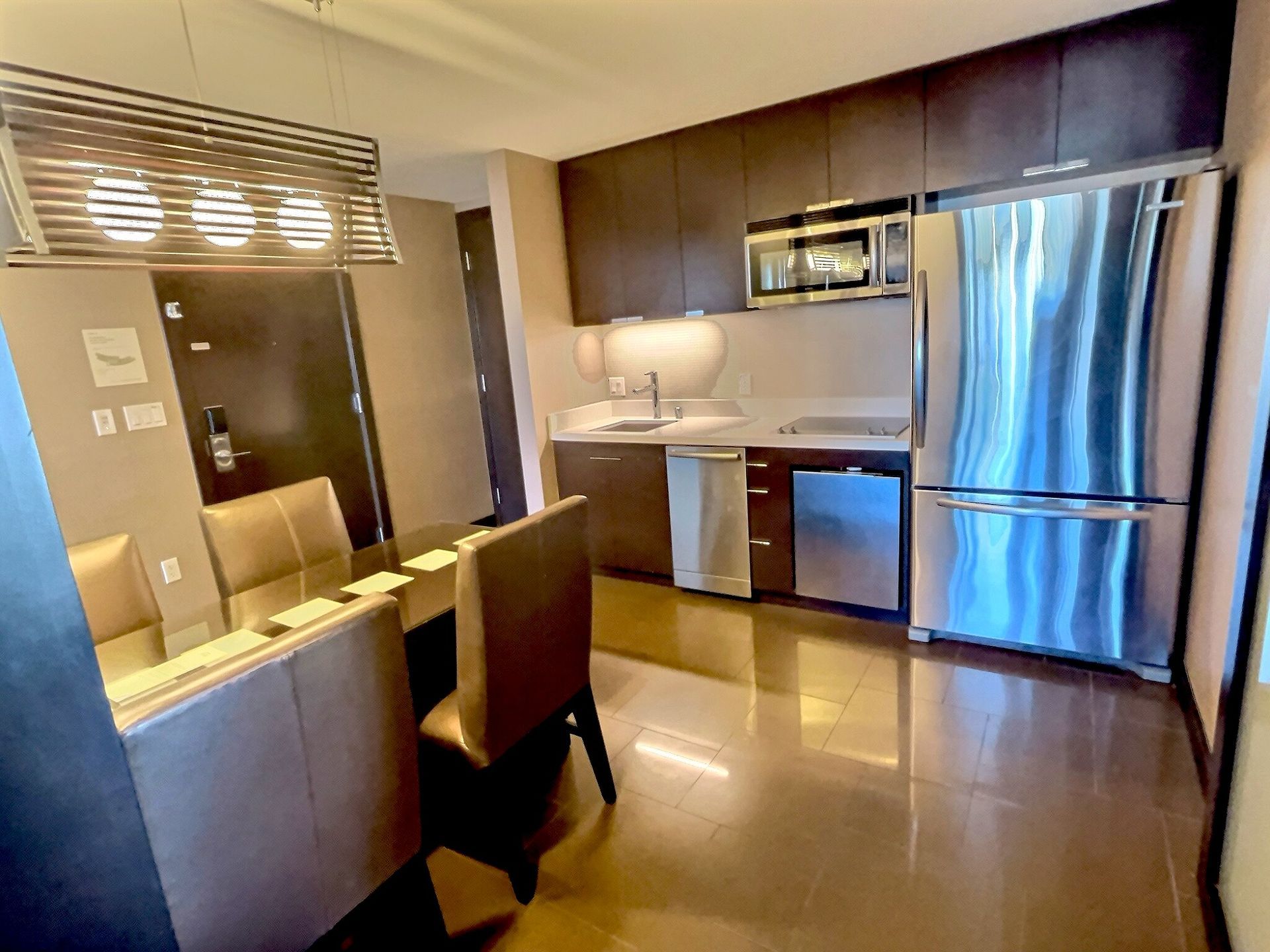 Modern kitchen and dining area with stainless steel appliances and wood table under warm lighting