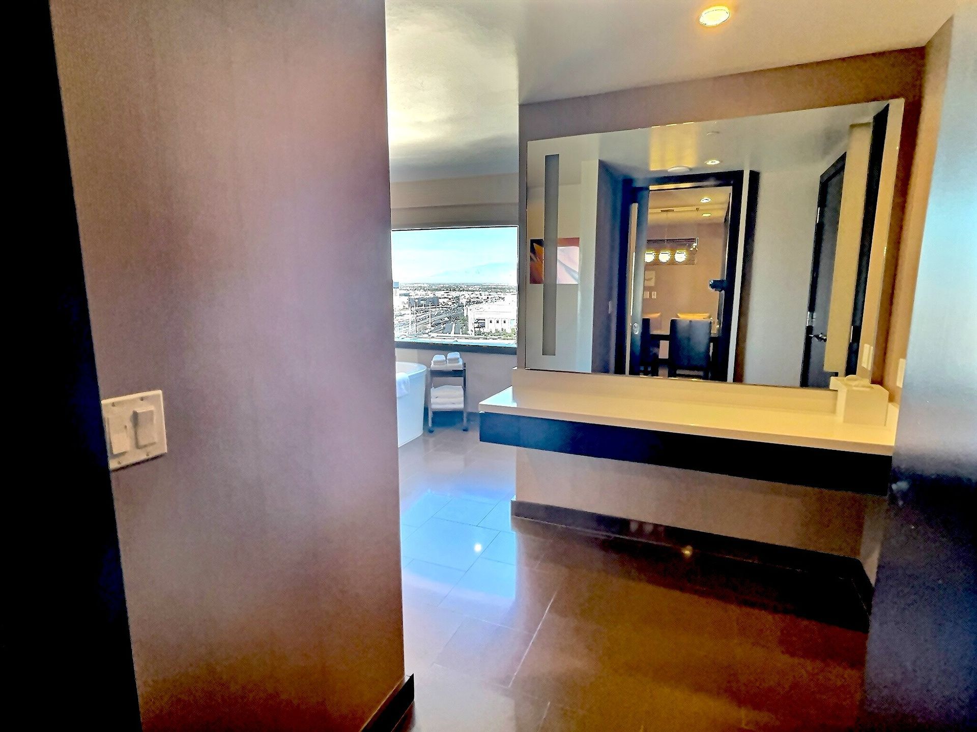 Modern hotel room with large mirror, desk, and city view through a bright window