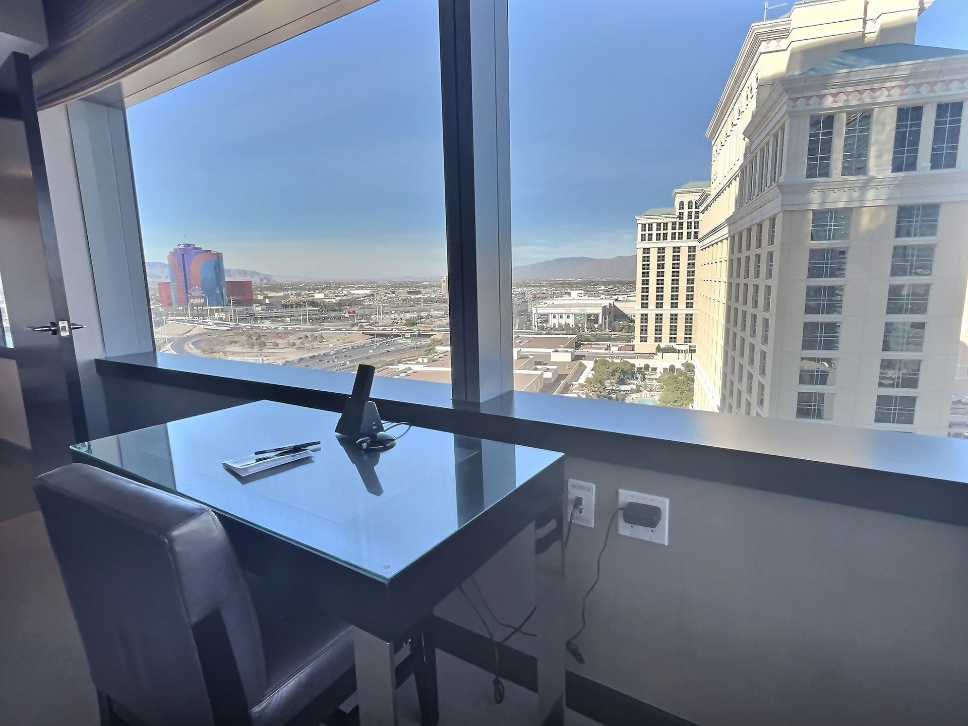 Glass-walled dining area with table by a large window overlooking a city skyline and mountains