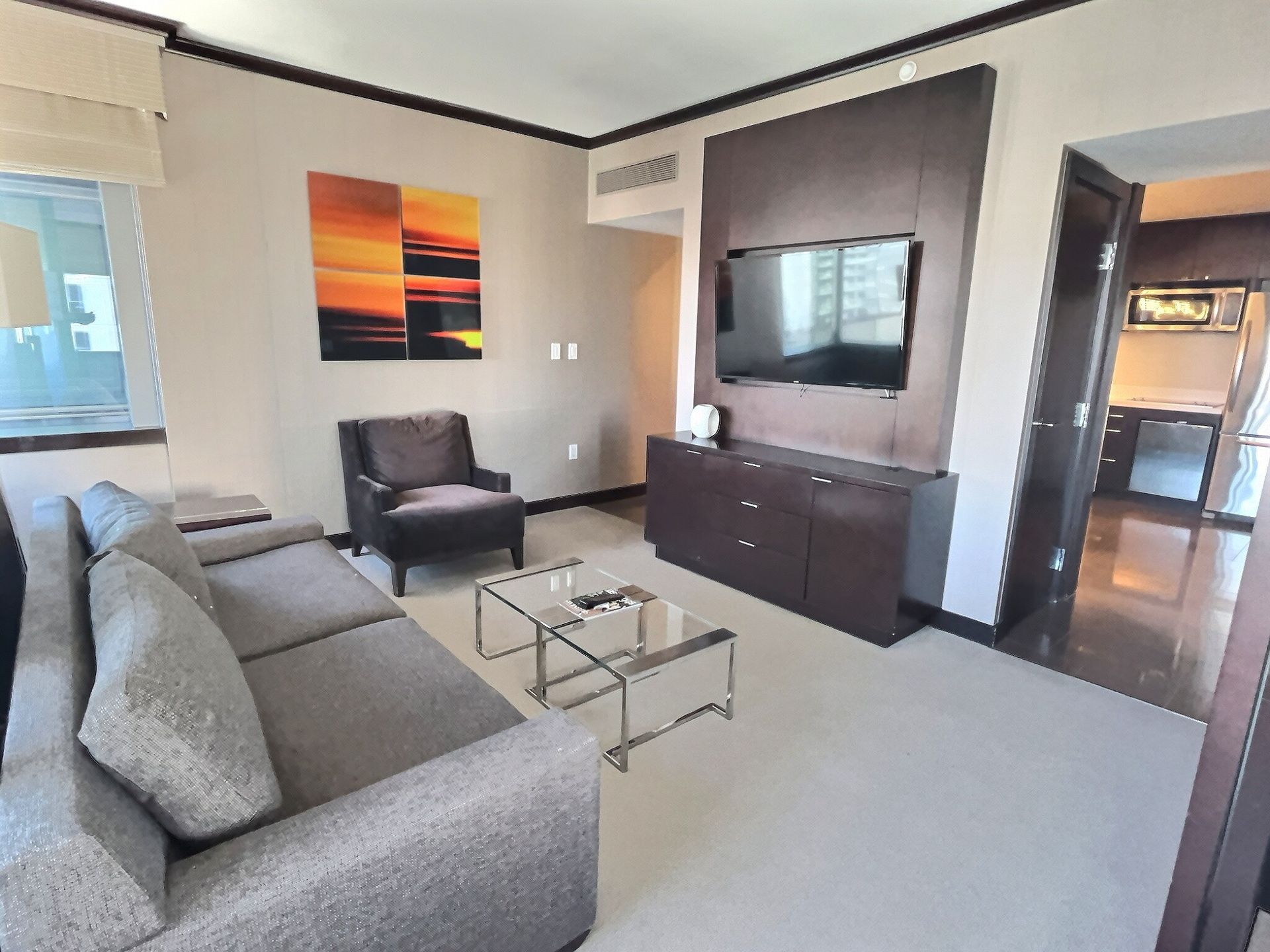 Modern living room with gray sofa, chair, glass coffee table, TV stand, and wall art.