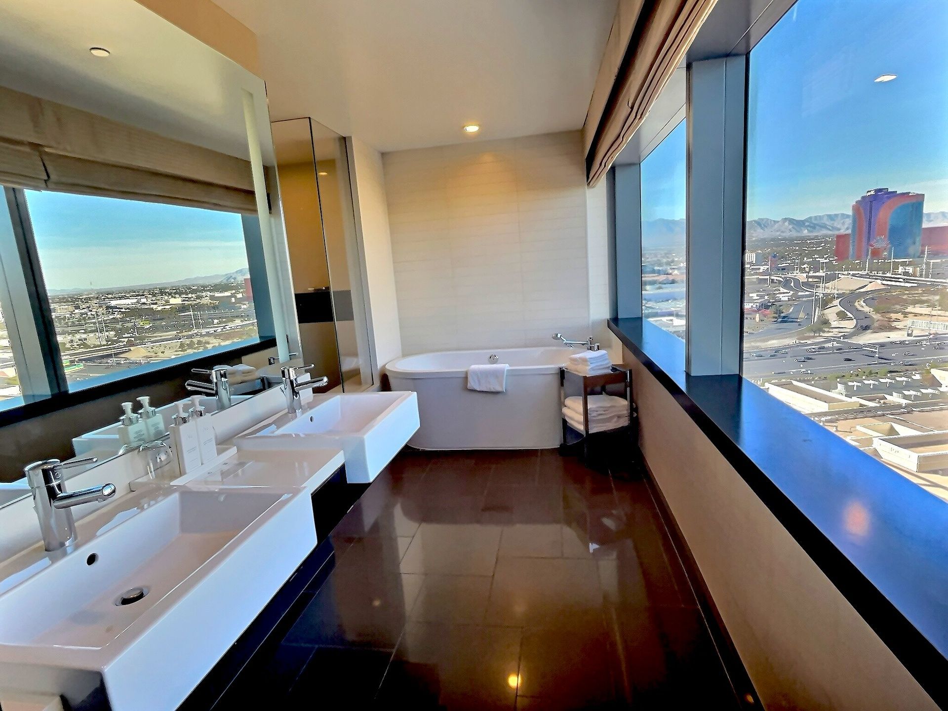 Modern bathroom with twin sinks and a large window overlooking a city skyline.
