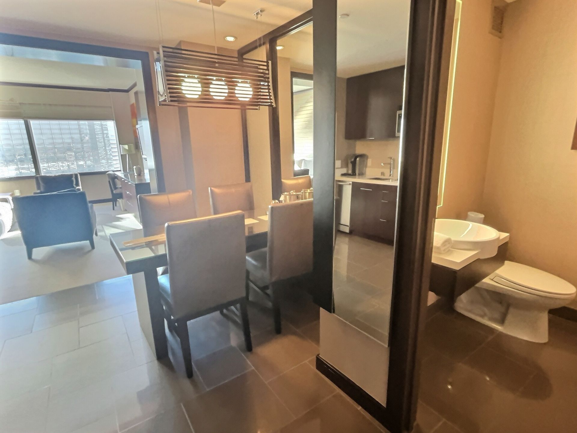 Modern hotel room with dining table, seating area, bed, and bathroom visible through a glass partition