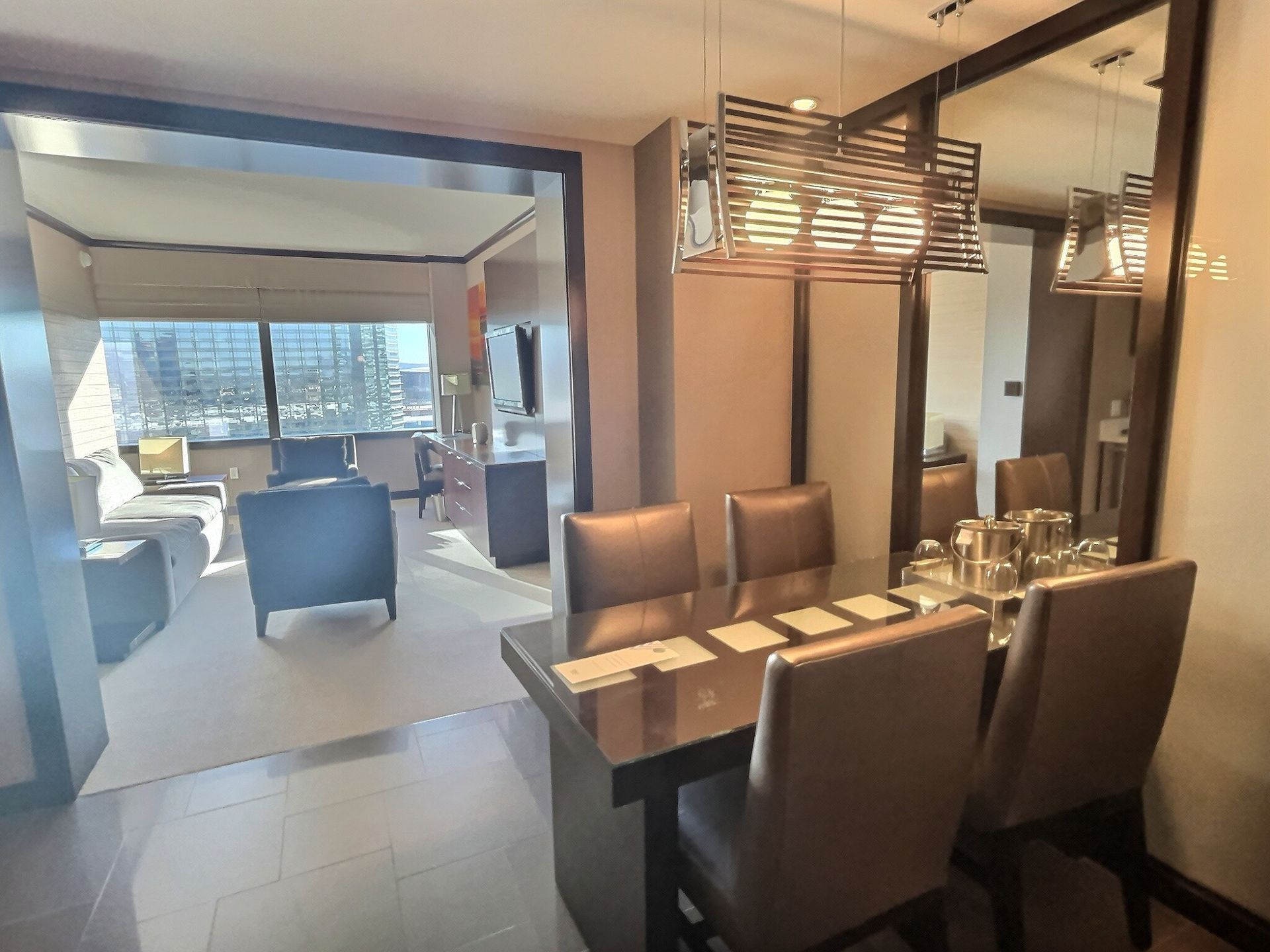 Modern dining area with a glass table, brown chairs, and a view into a bright living room beyond