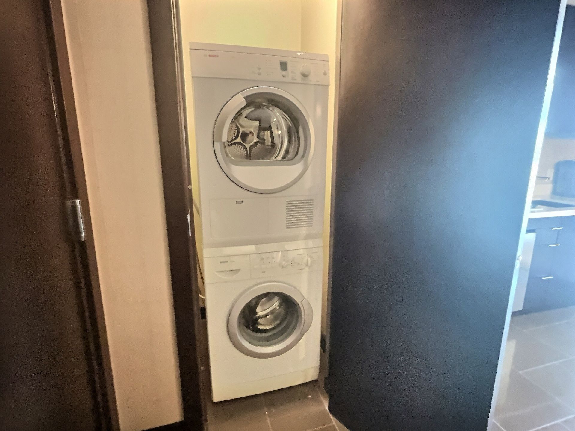 Stacked washer and dryer in a narrow doorway, with a dark door open beside them.