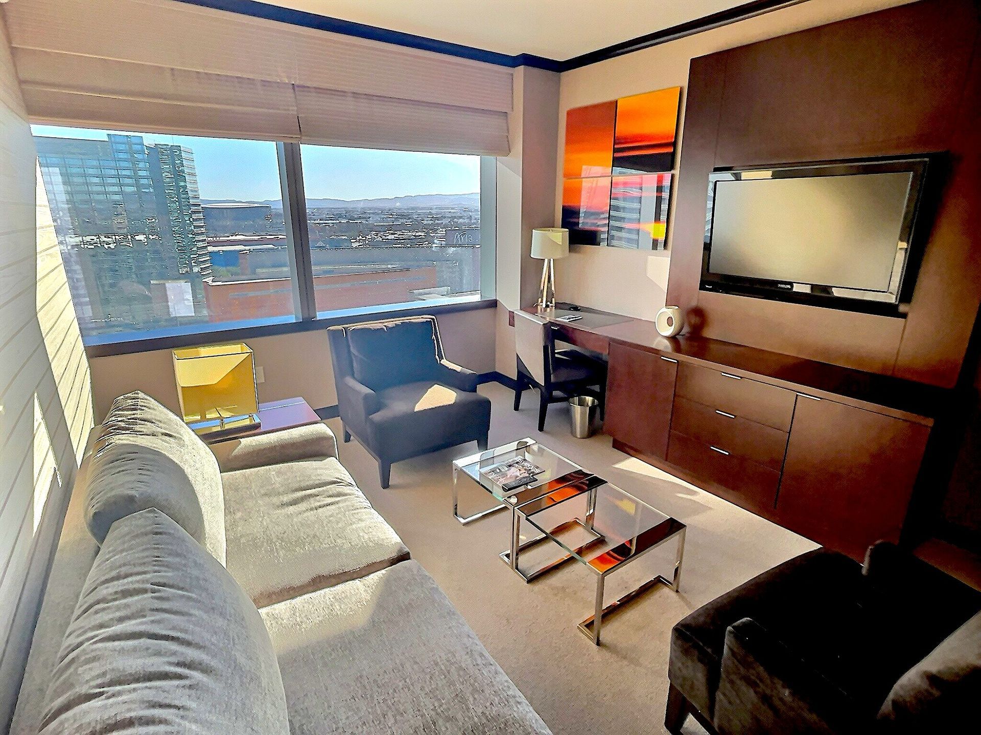 Modern living room with sofa, armchairs, coffee table, wall TV, and city view through large windows