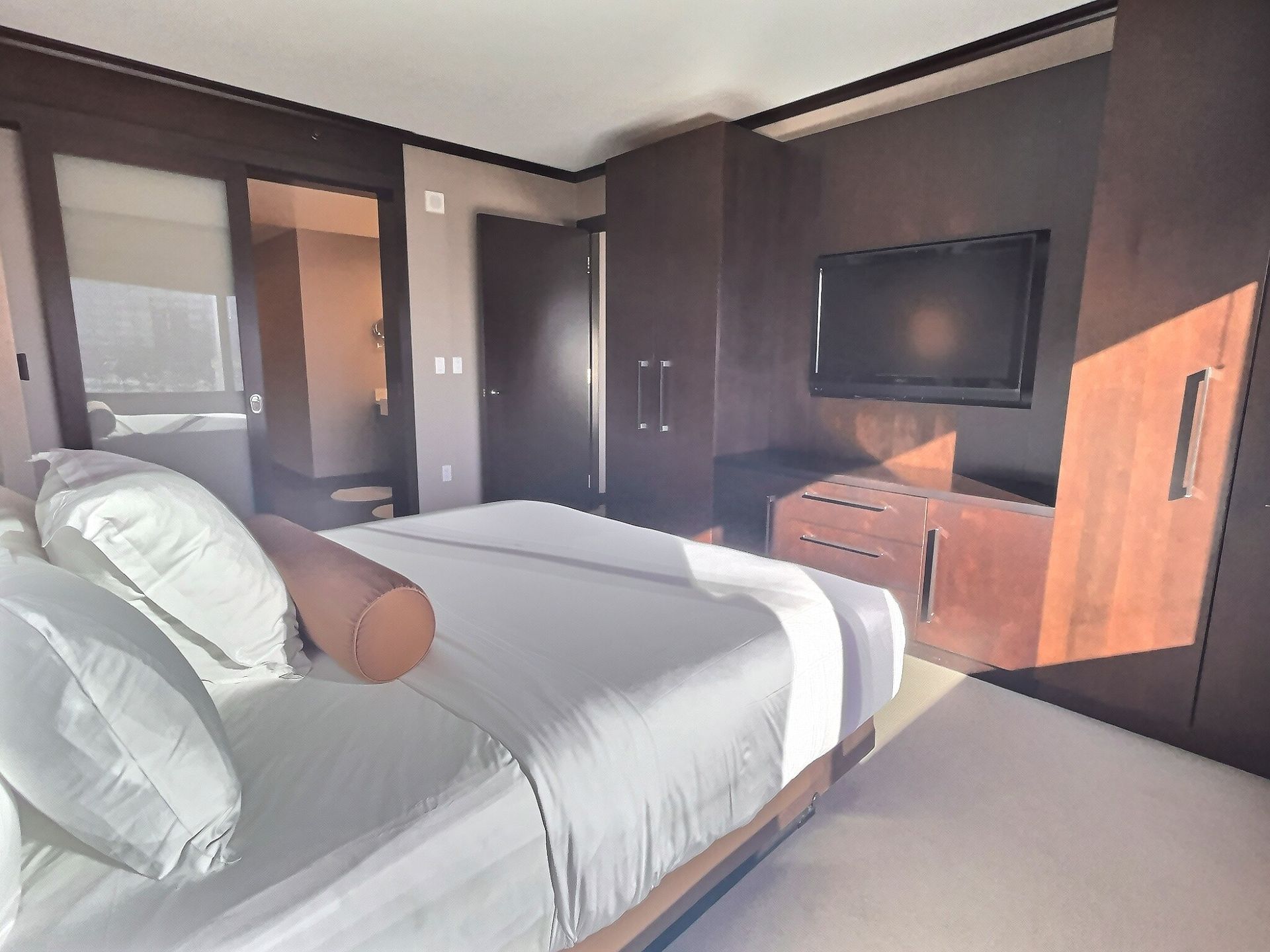 Modern bedroom with a large bed, TV on a dresser, and sunlight streaming through the window.