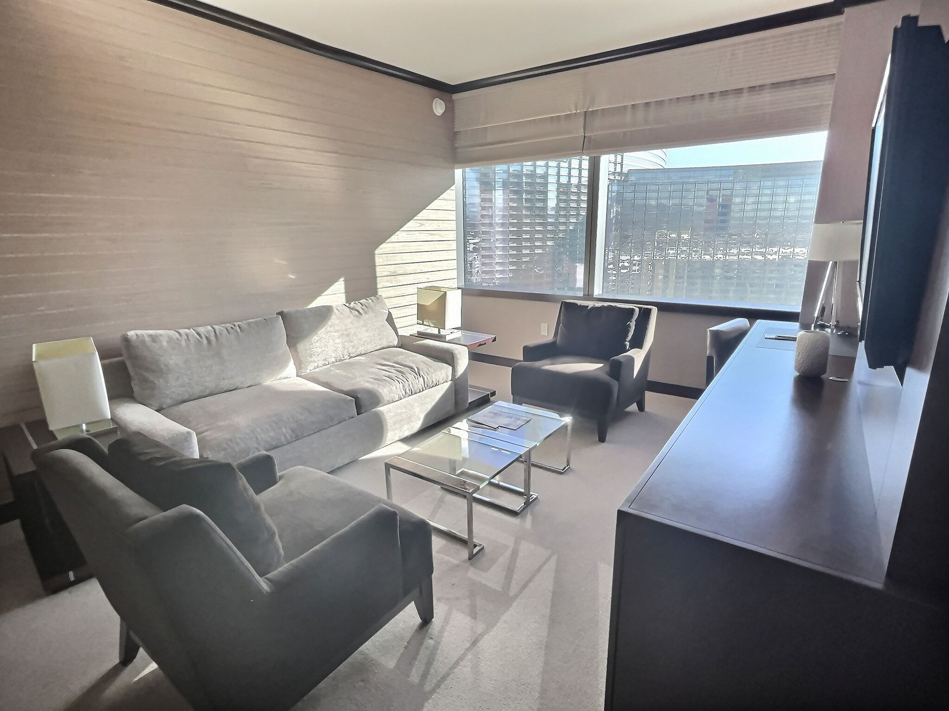 Modern living room with gray sofa, black chairs, glass coffee table, TV console, and large bright window