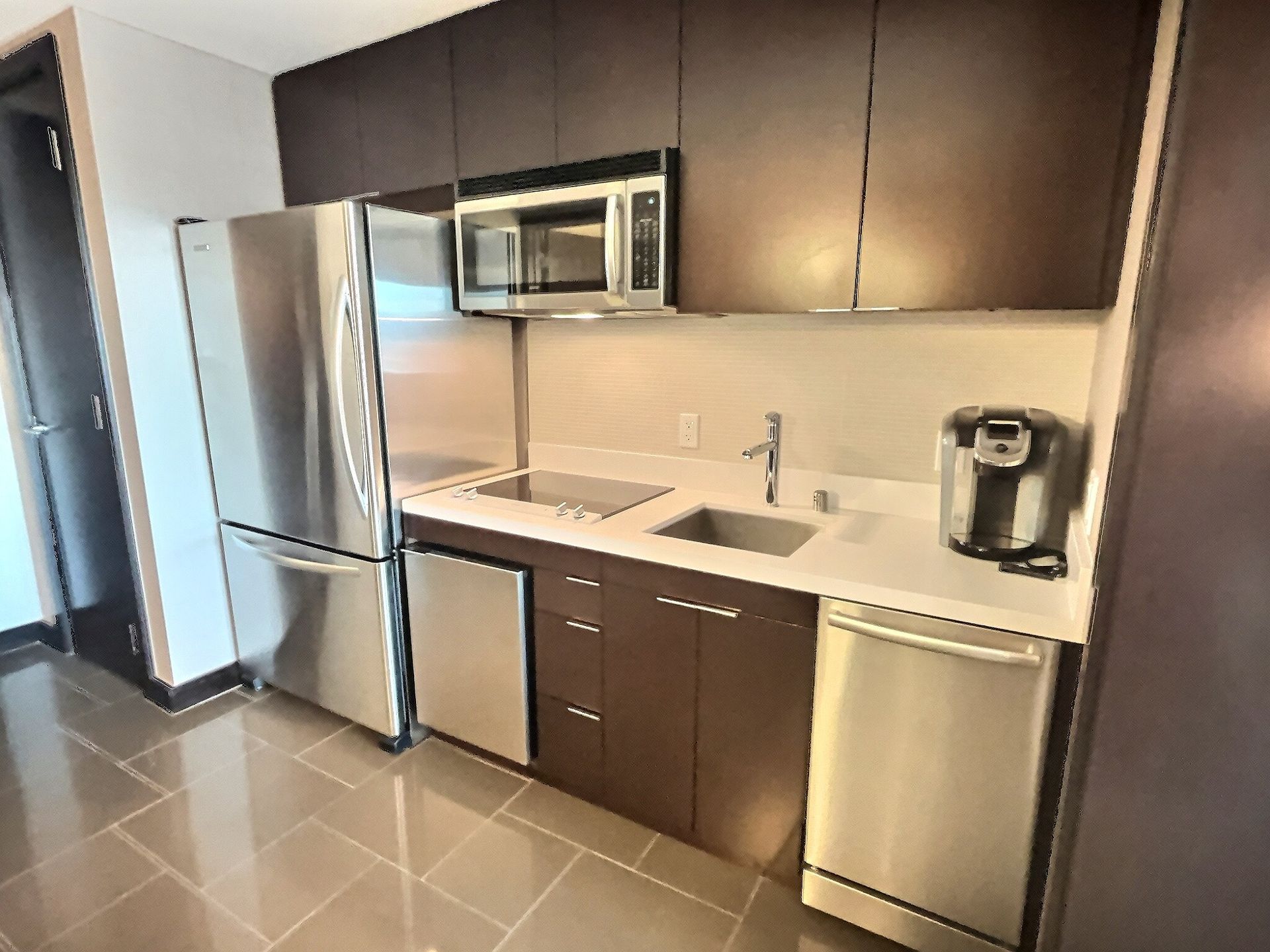 Modern kitchen with stainless steel appliances, dark cabinets, and glossy tile floor
