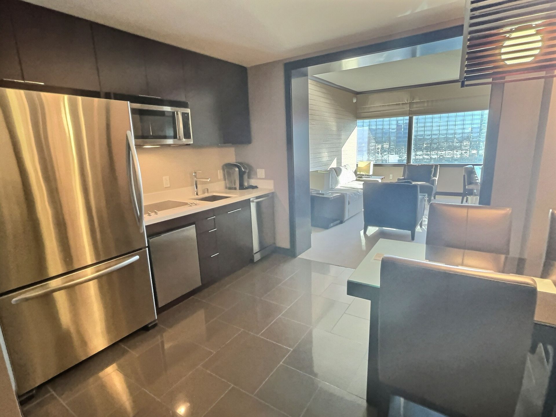 Modern kitchen with stainless steel appliances, tiled floor, and a bright dining area beyond.