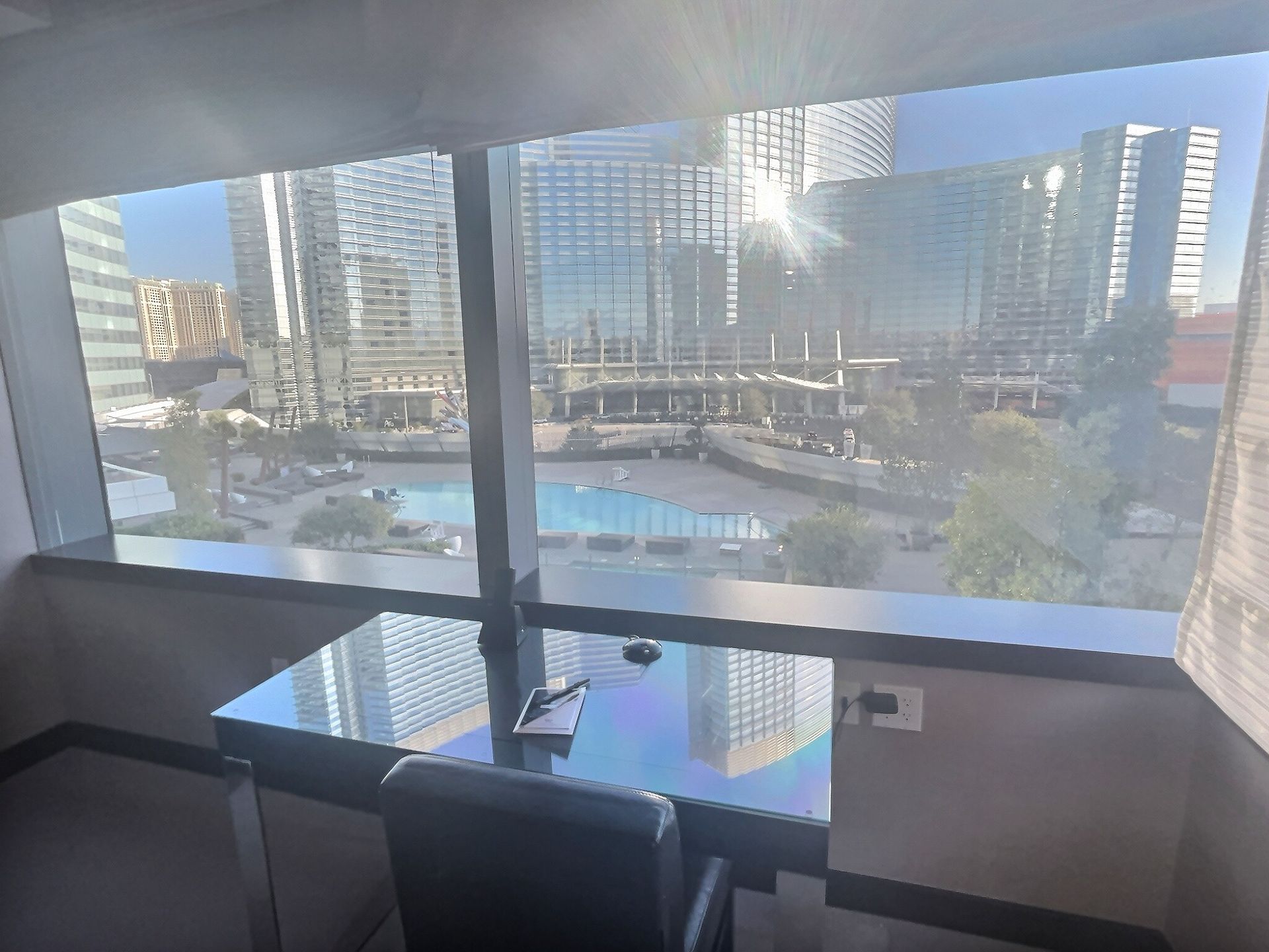 Hotel room desk and chair facing a balcony with a city skyline and pool view