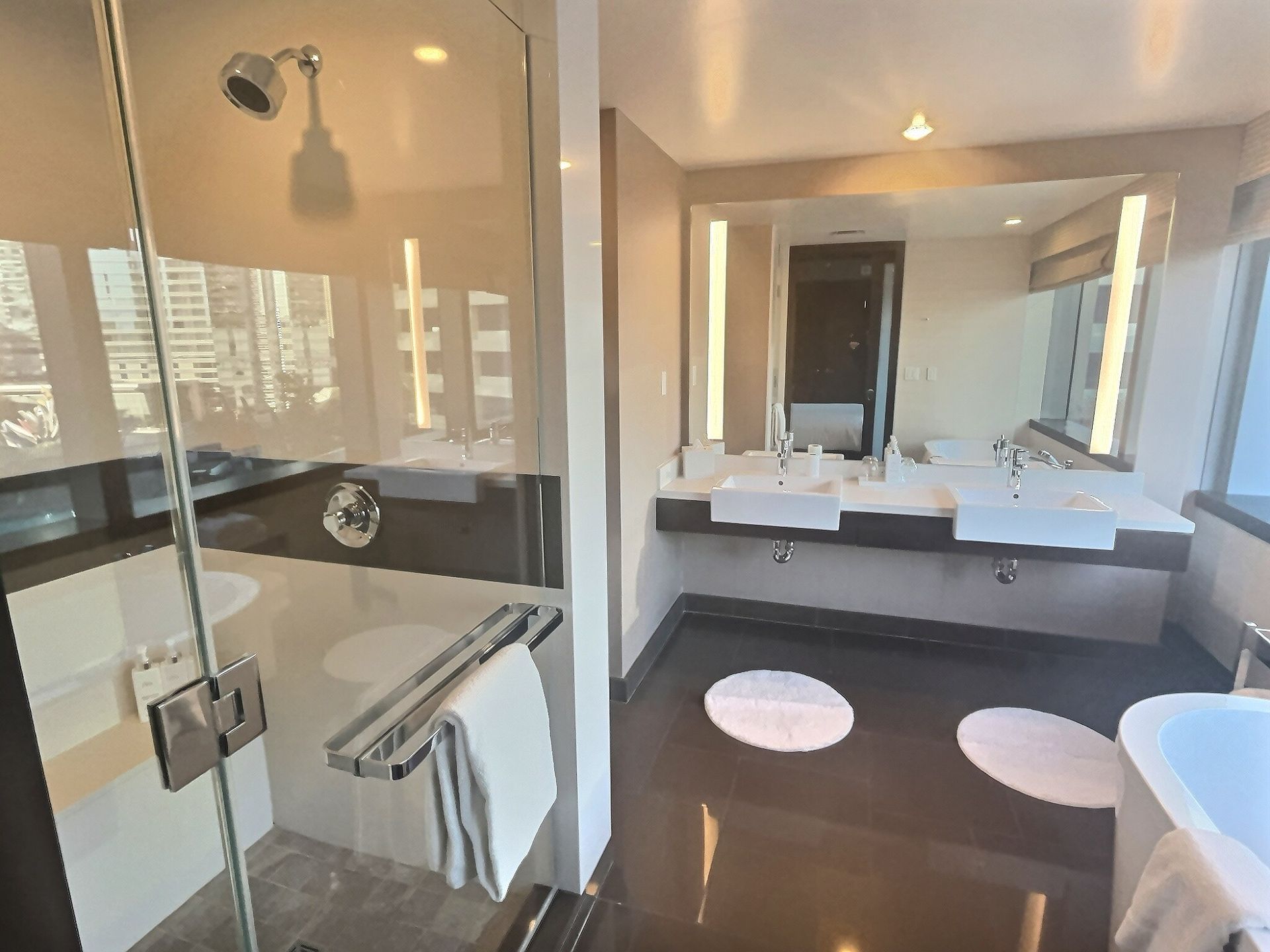 Modern bathroom with glass shower, vanity, large mirror, dark flooring, and bathtub by the window