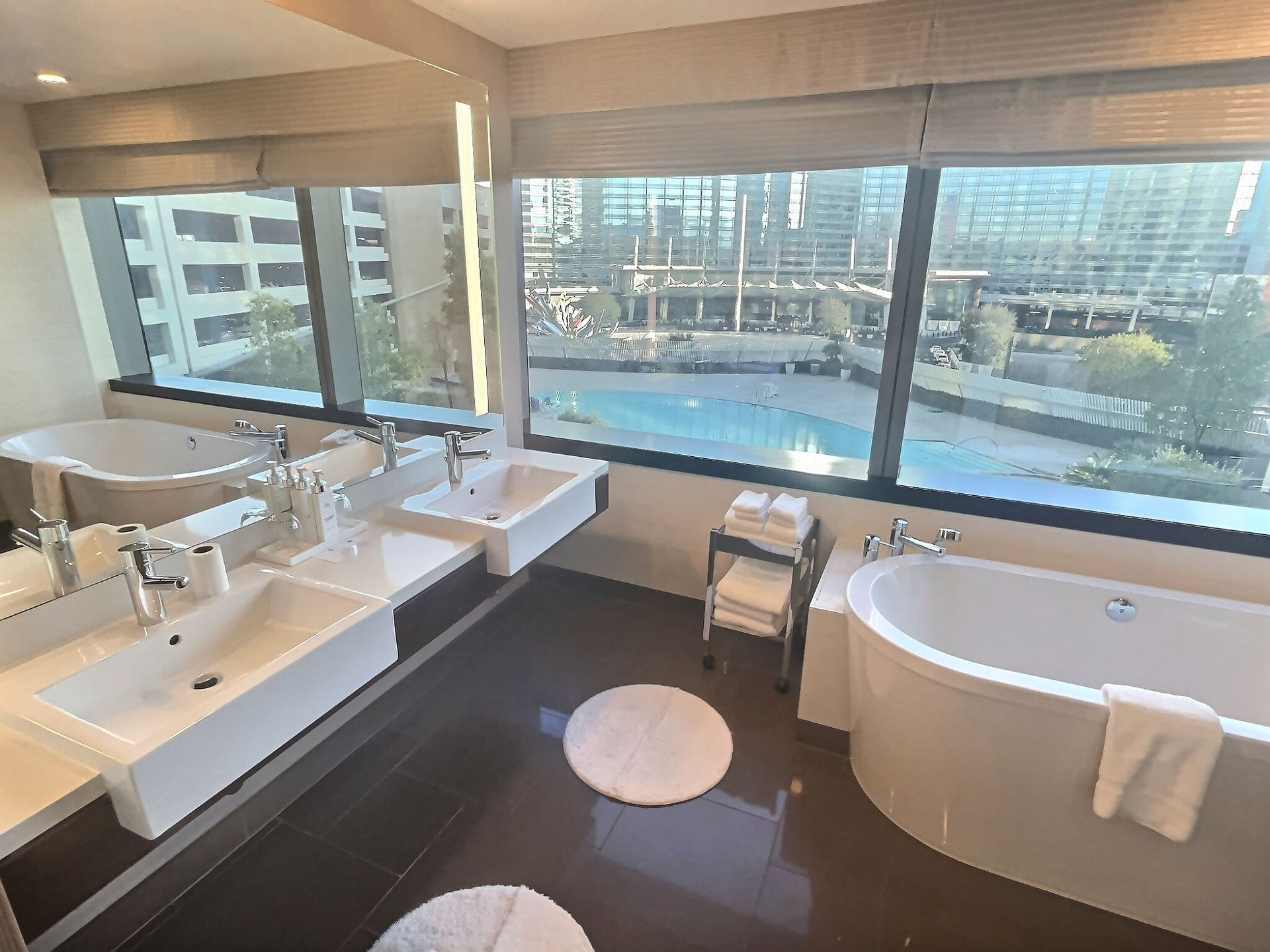 Modern bathroom with double vanity, freestanding tub, and city-view window overlooking a pool