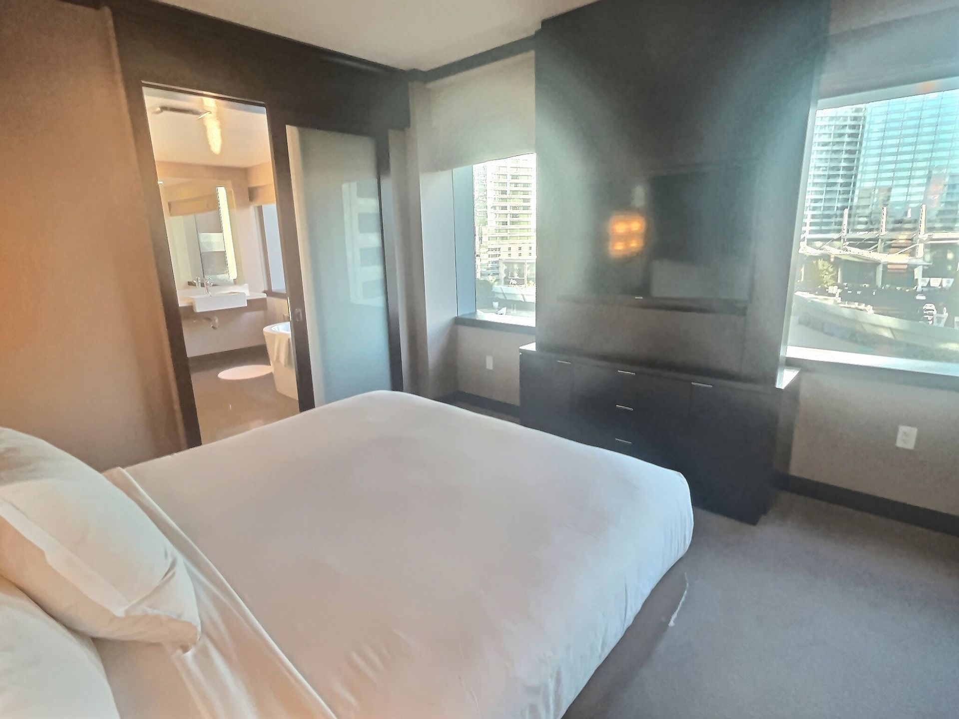 Modern bedroom with white bed, dark accent wall, windows, and a wall-mounted TV