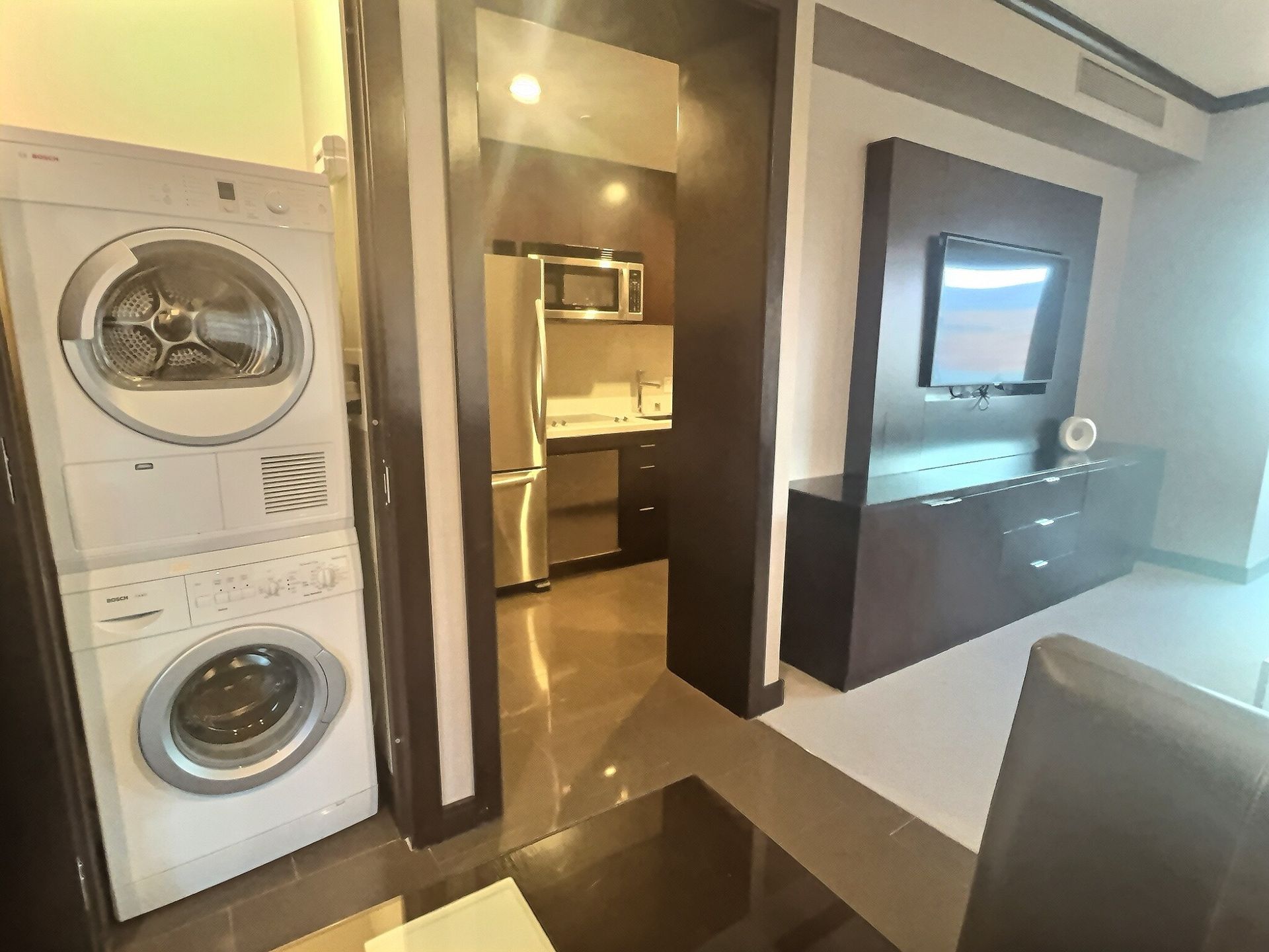 Modern apartment interior with stacked washer-dryer, kitchen doorway, and TV console with a wall-mounted TV