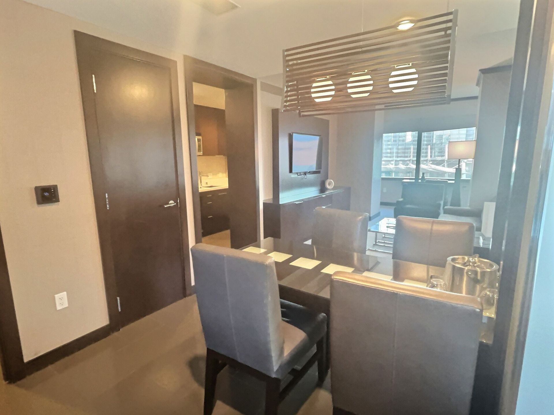 Modern hotel room with desk, chair, TV, and large window overlooking the city.